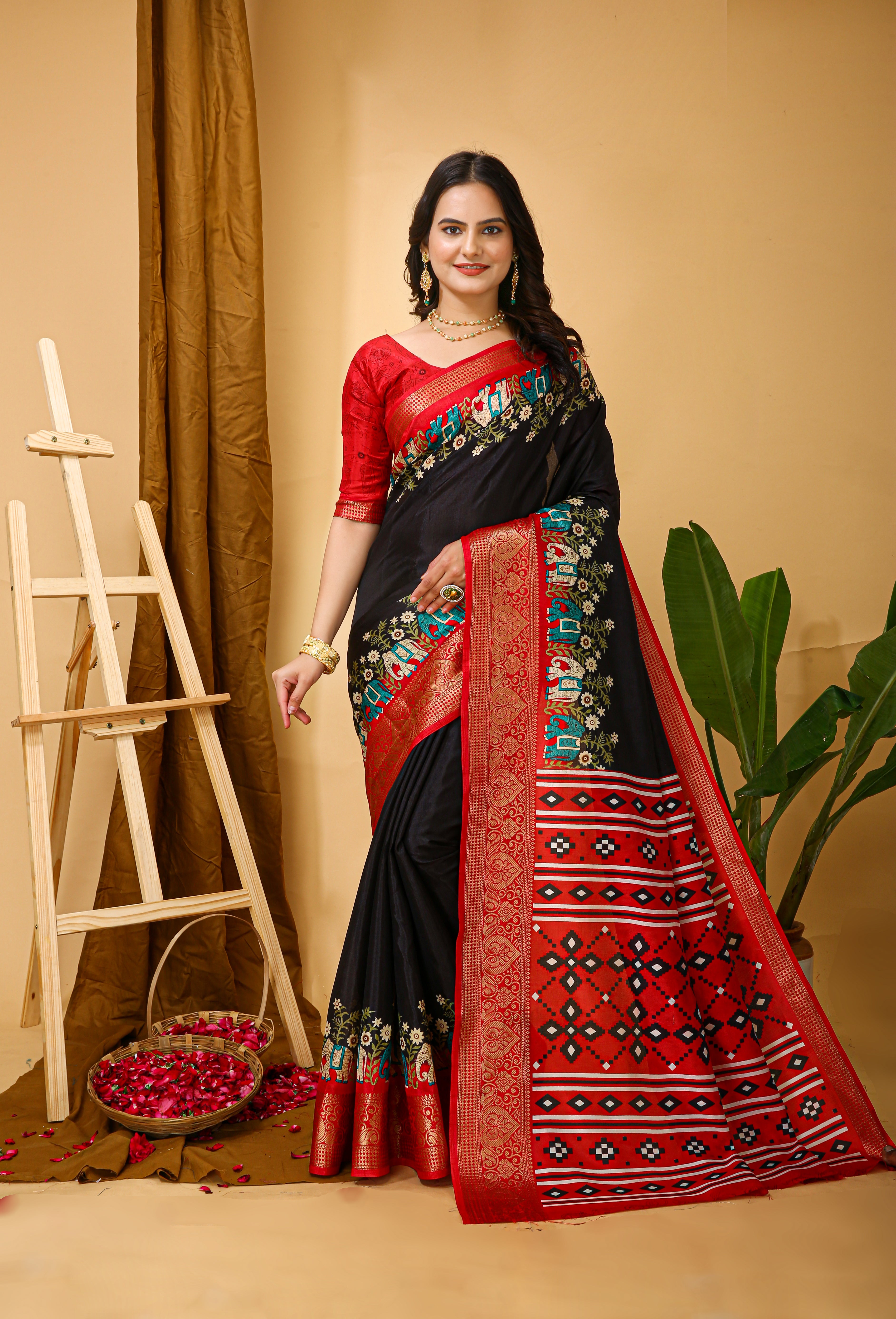 Woman wearing a black and red saree with floral patterns in a decorated indoor setting.