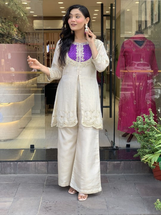 Woman in a white and purple traditional outfit standing in front of a store window with clothing displays.