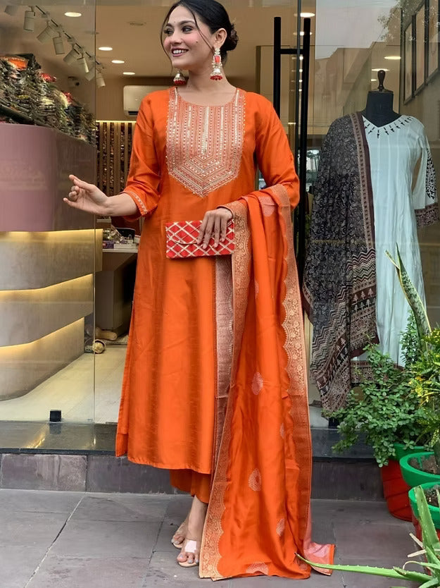 Woman in an orange traditional outfit standing in front of a store entrance.