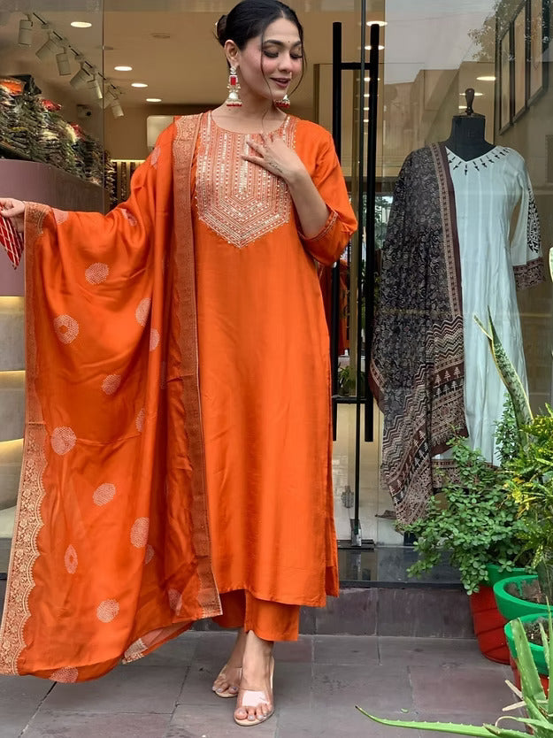 Woman in an orange traditional outfit standing in front of a store window displaying more clothing.