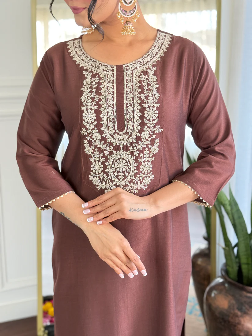 Brown dress with white embroidery worn by a person, with a blurred indoor background.