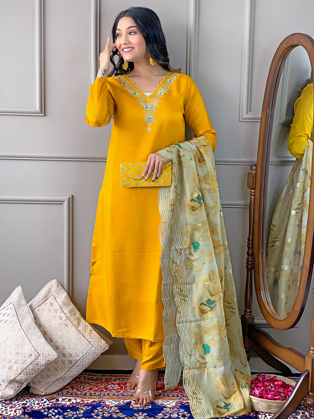 Woman in a yellow traditional outfit standing next to a mirror, holding a floral dupatta.