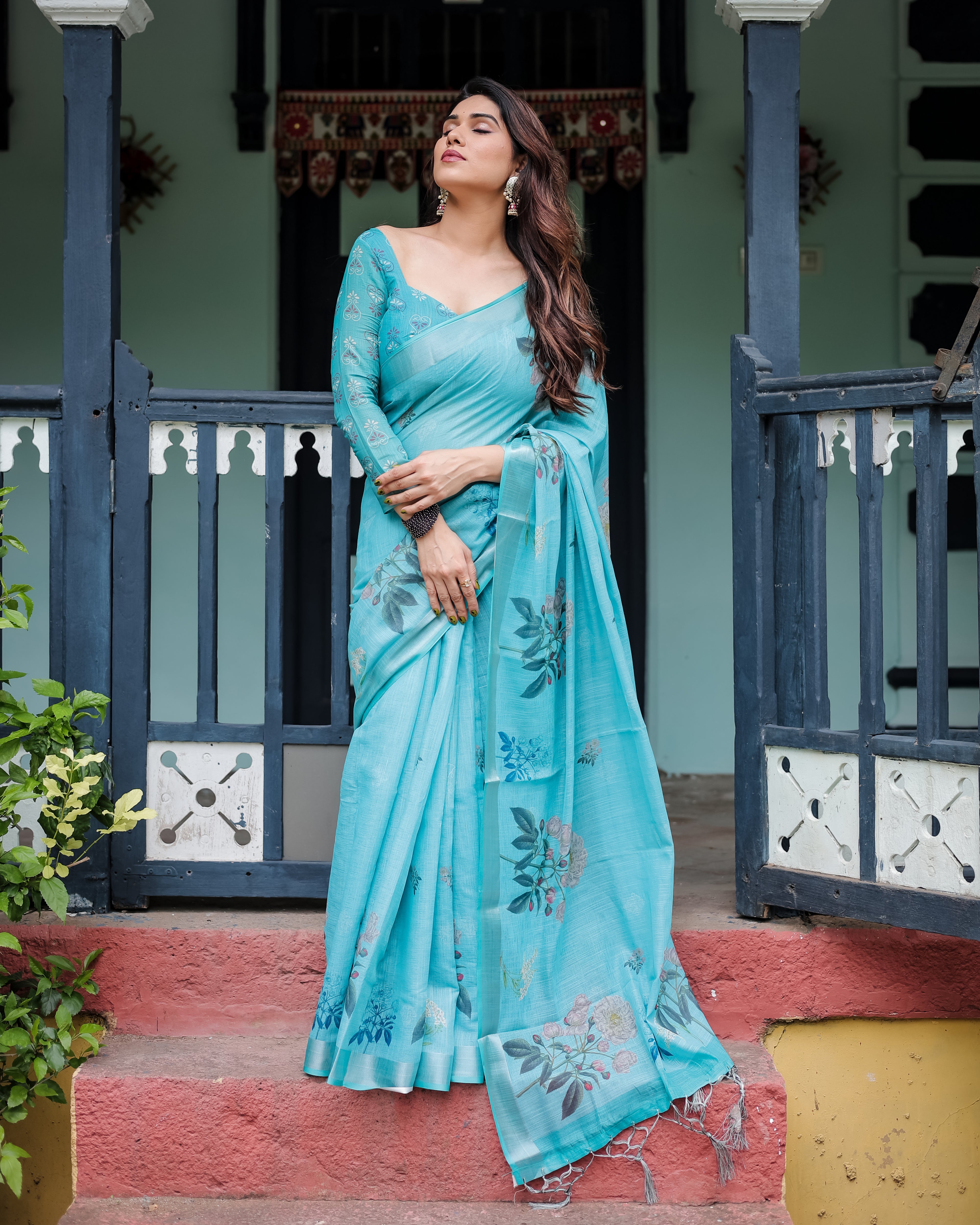 Woman in a turquoise saree standing on steps with a traditional setting in the background