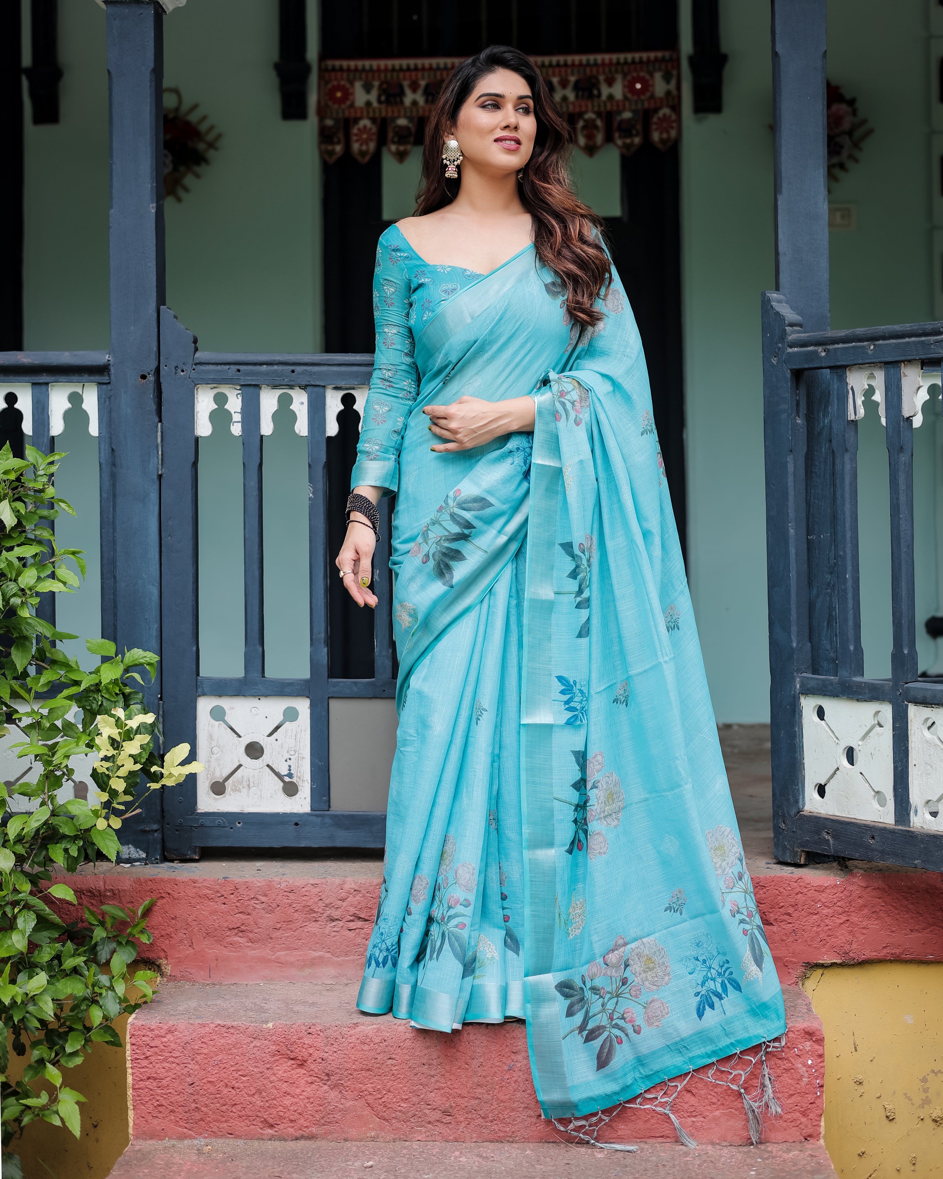 Woman in a light blue saree standing on steps with a decorative background