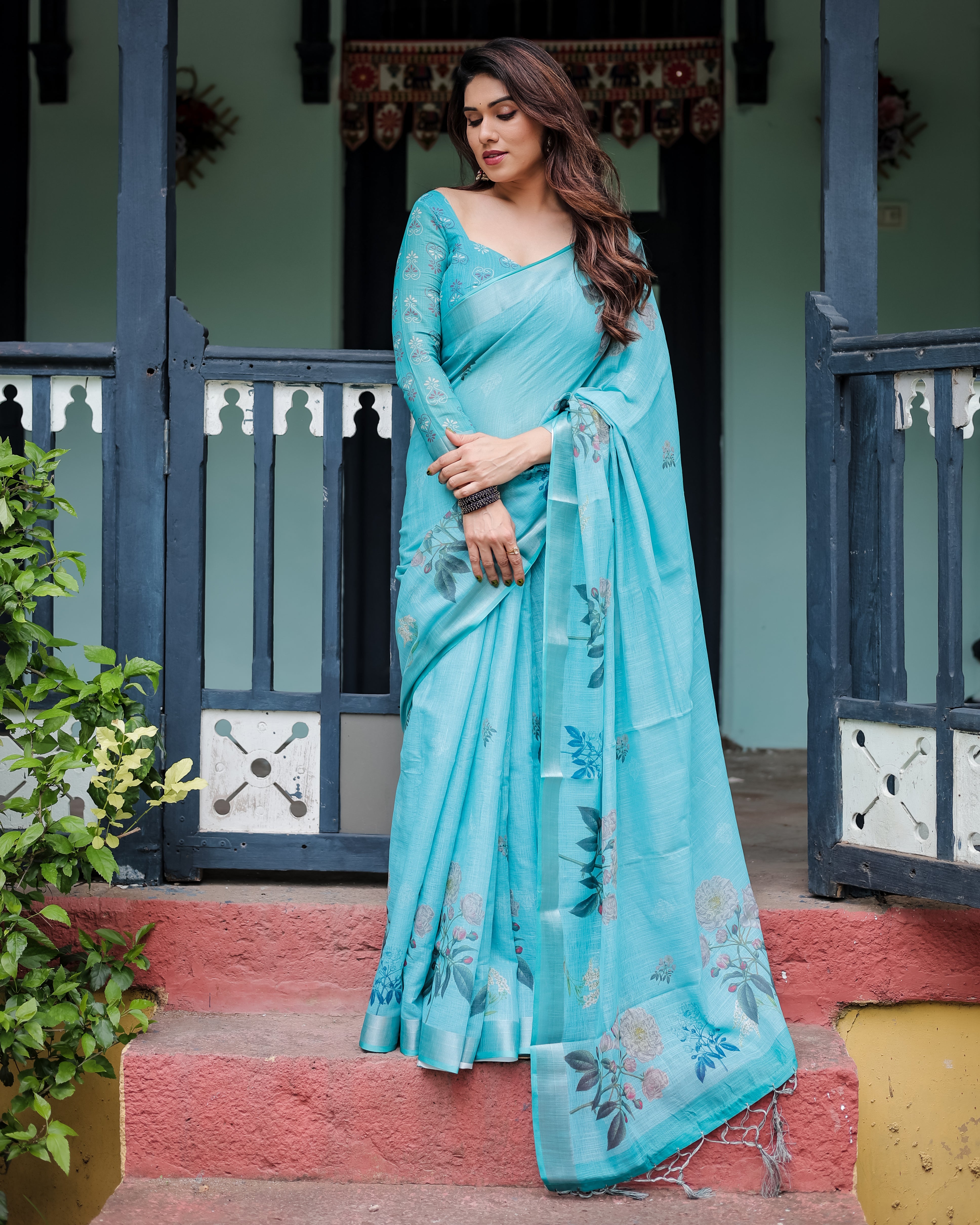 Woman in a light blue saree standing outdoors with a decorative background