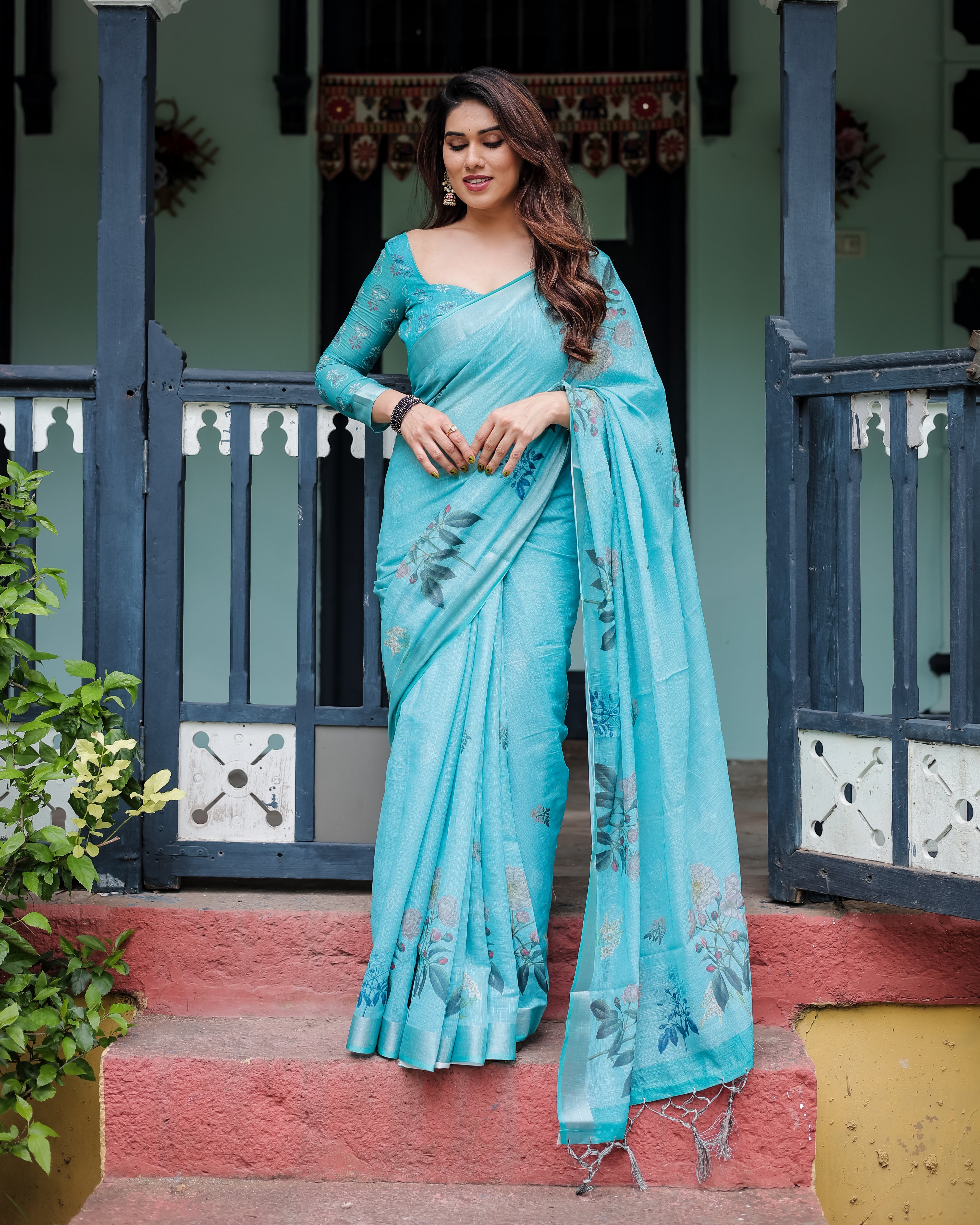 Woman in a light blue saree standing on steps with a decorative background