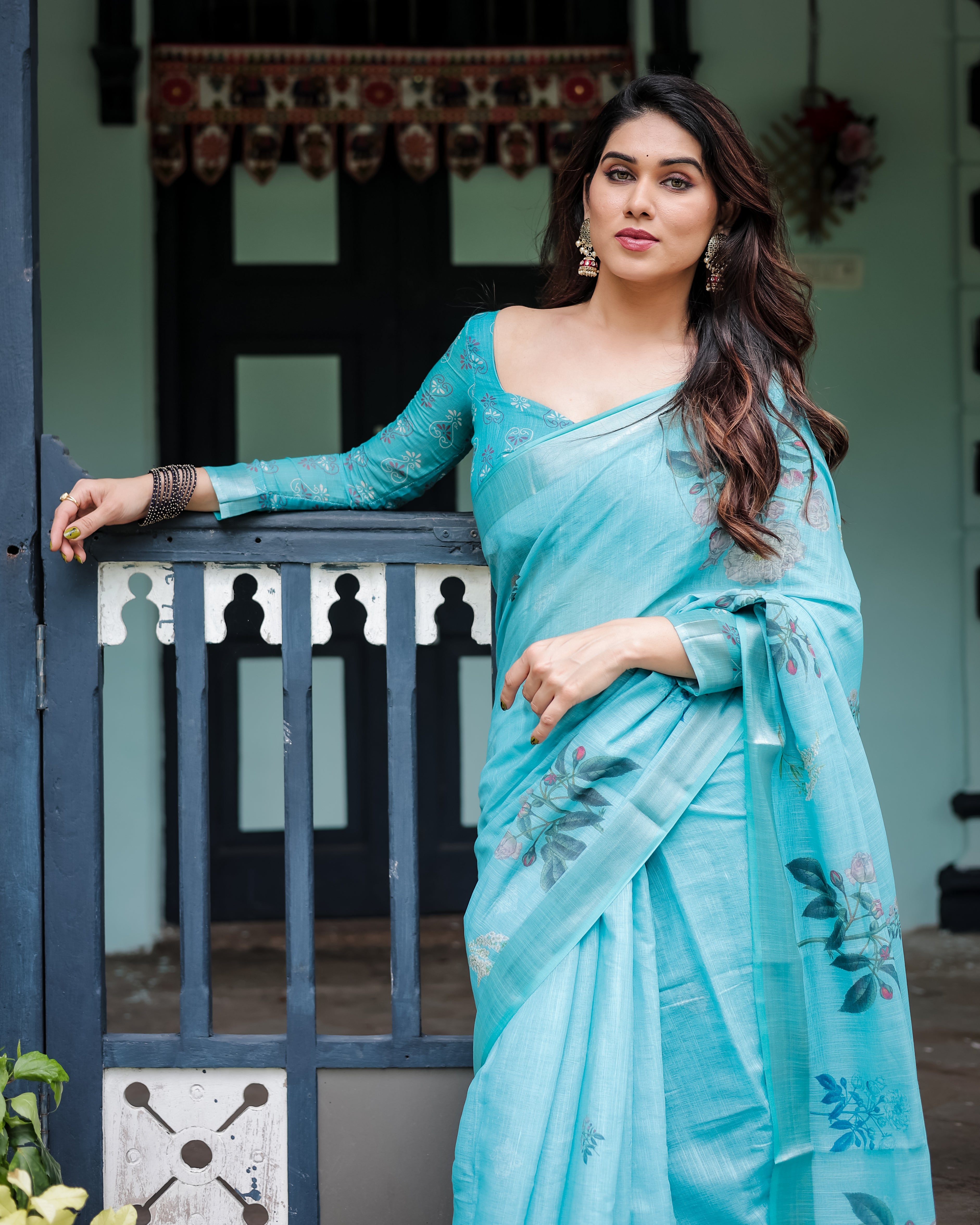 Woman in a aqua blue saree standing in front of a decorative door.