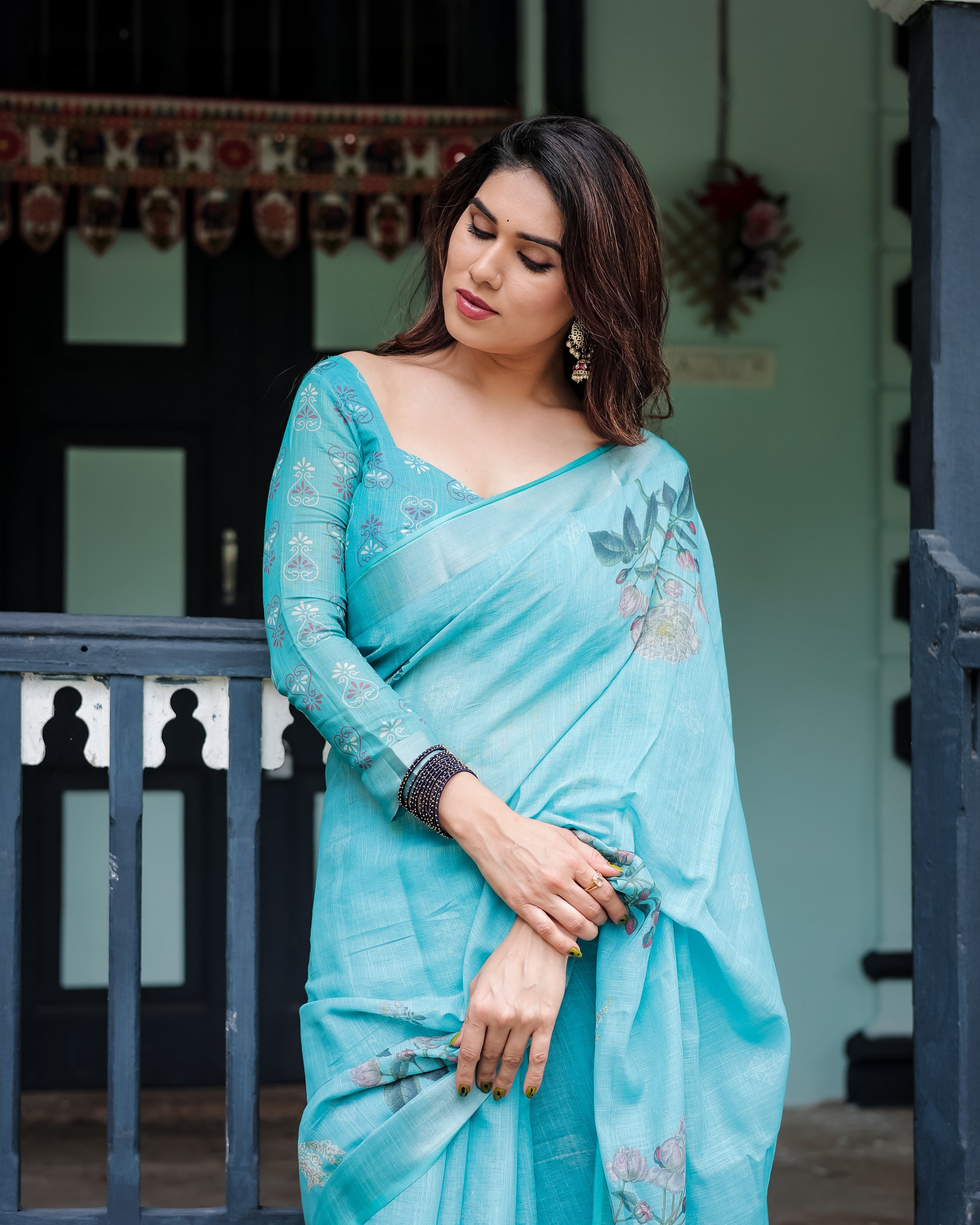 Woman wearing a aqua blue saree with floral patterns in an outdoor setting.