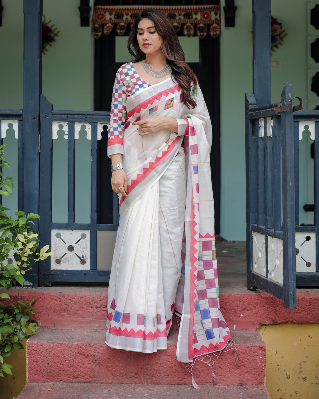 Woman wearing a white saree with colorful patterns standing in front of a traditional building.