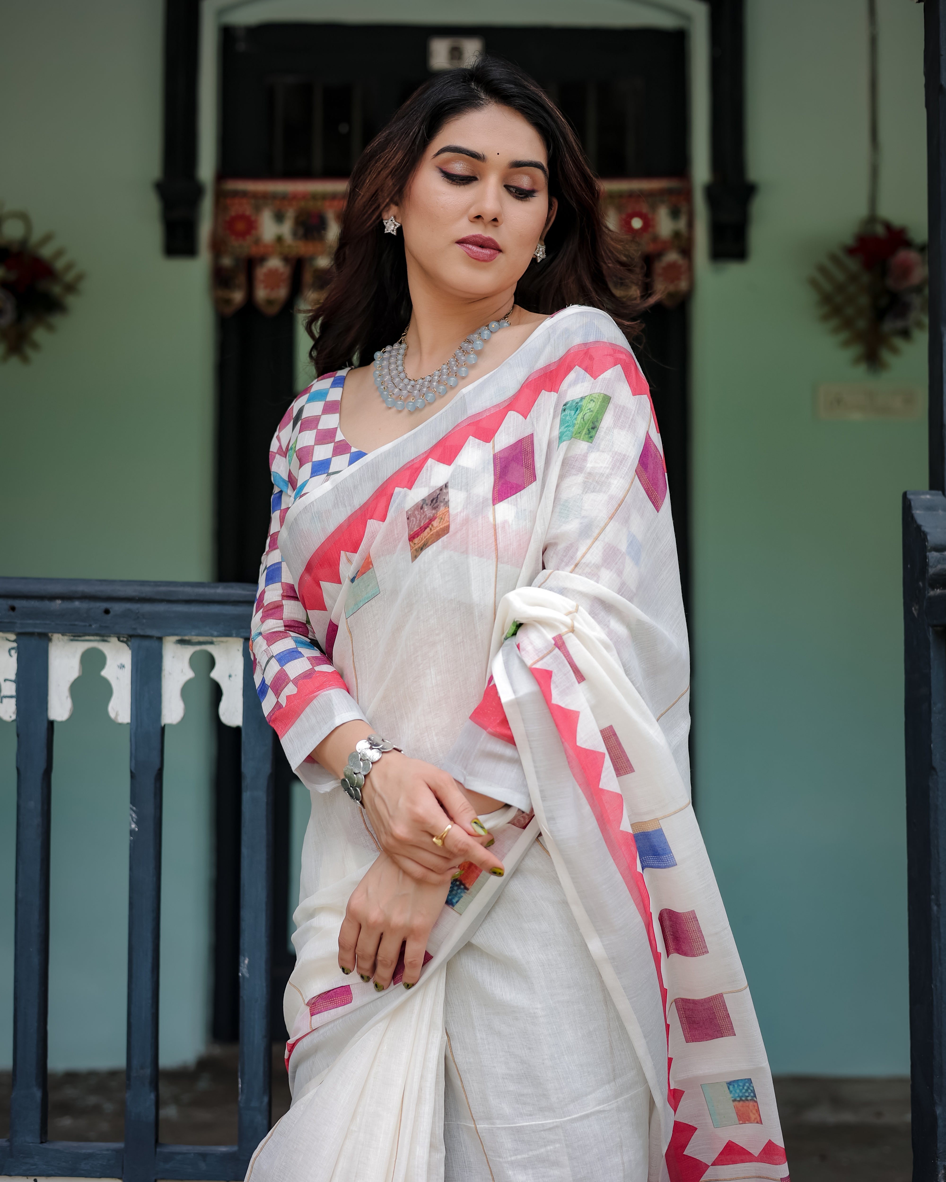 Woman wearing a white saree with colorful patterns in an outdoor setting