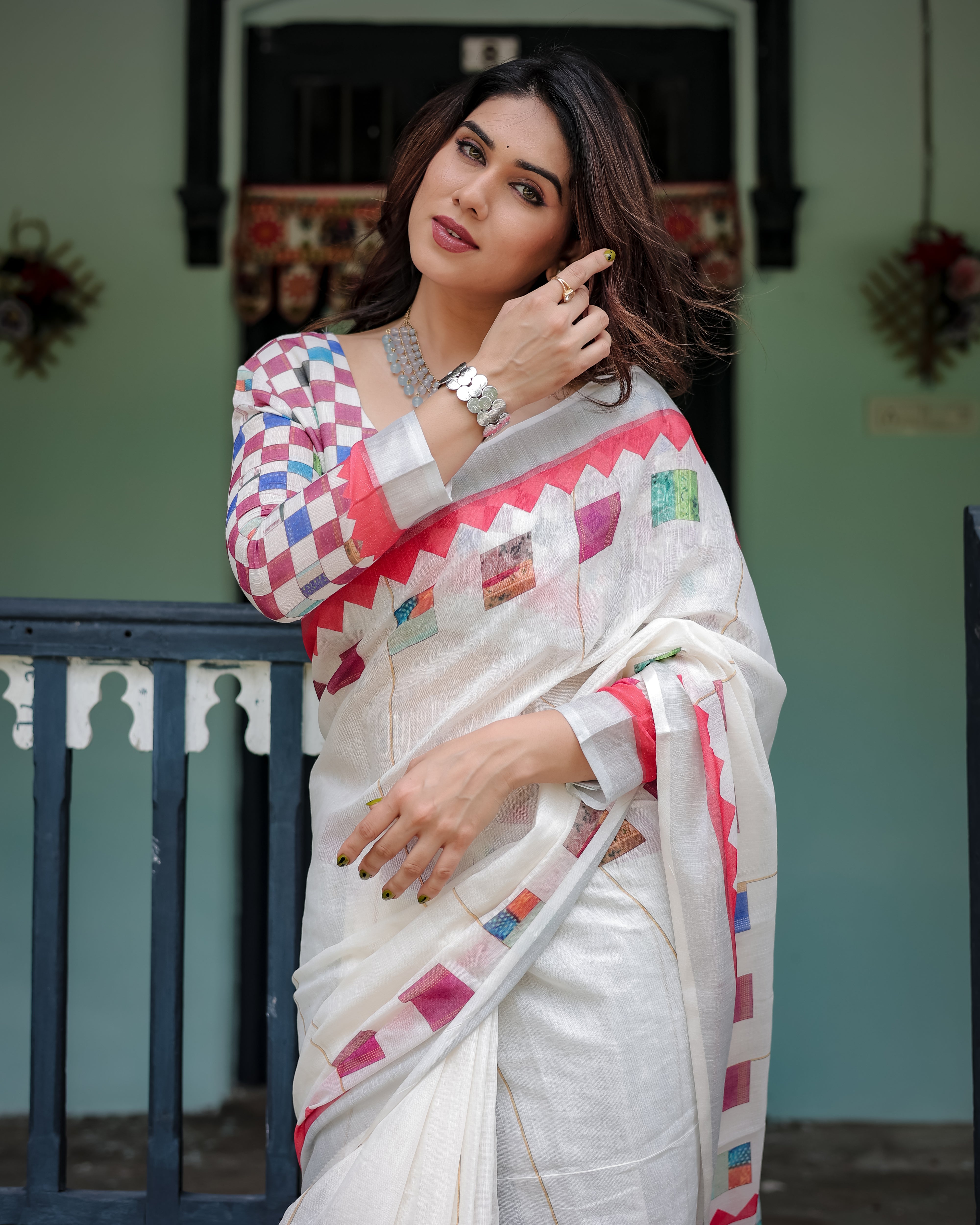 Woman wearing a white saree with colorful patterns in an outdoor setting.