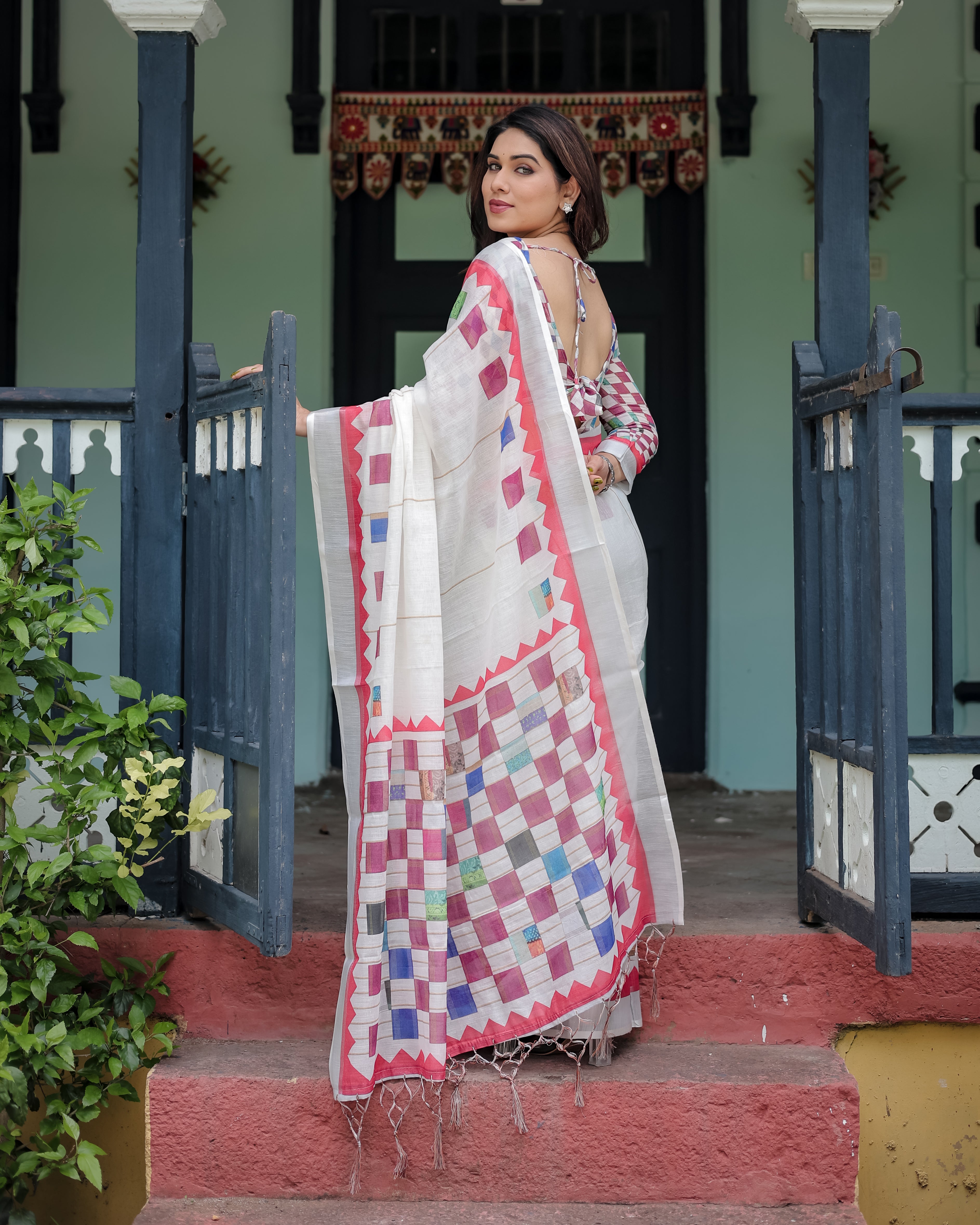 Woman in a traditional saree standing on steps with a decorative background