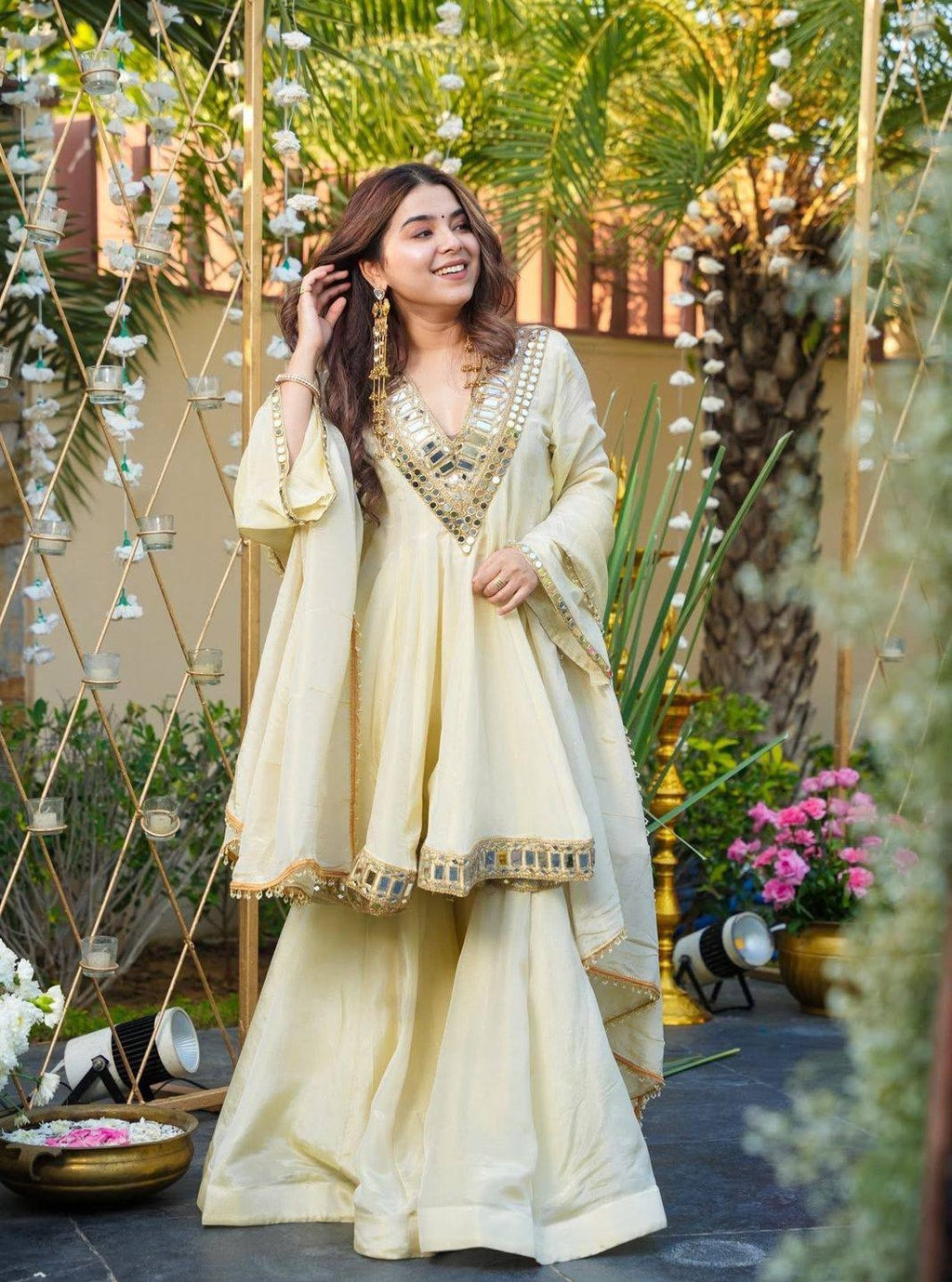 Woman in a traditional Kurta Plazo Set outfit standing outdoors with decorative elements and plants.