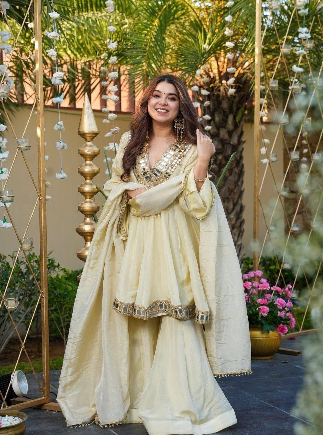 Woman in a traditional Kurta Plazo Set outfit standing outdoors with decorative elements and plants.