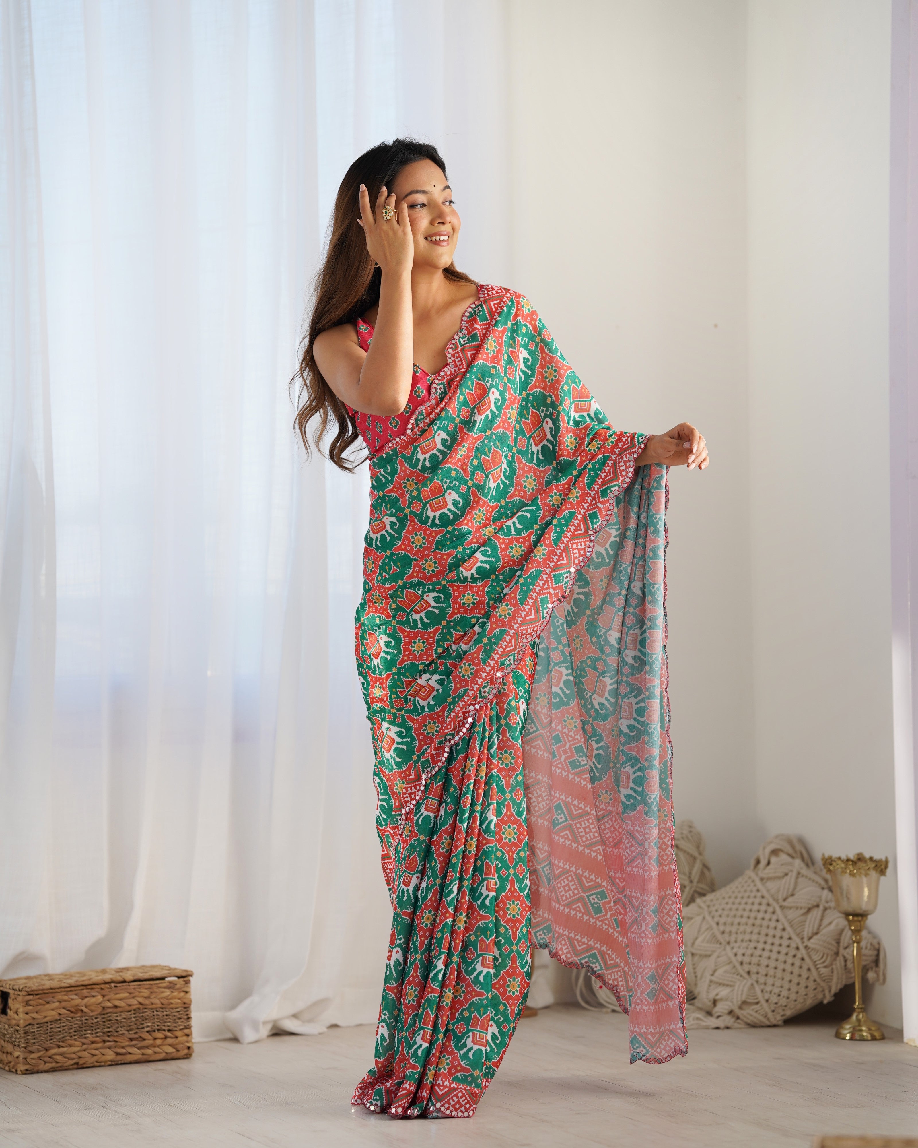 Woman wearing a colorful floral saree in a bright room with white curtains.