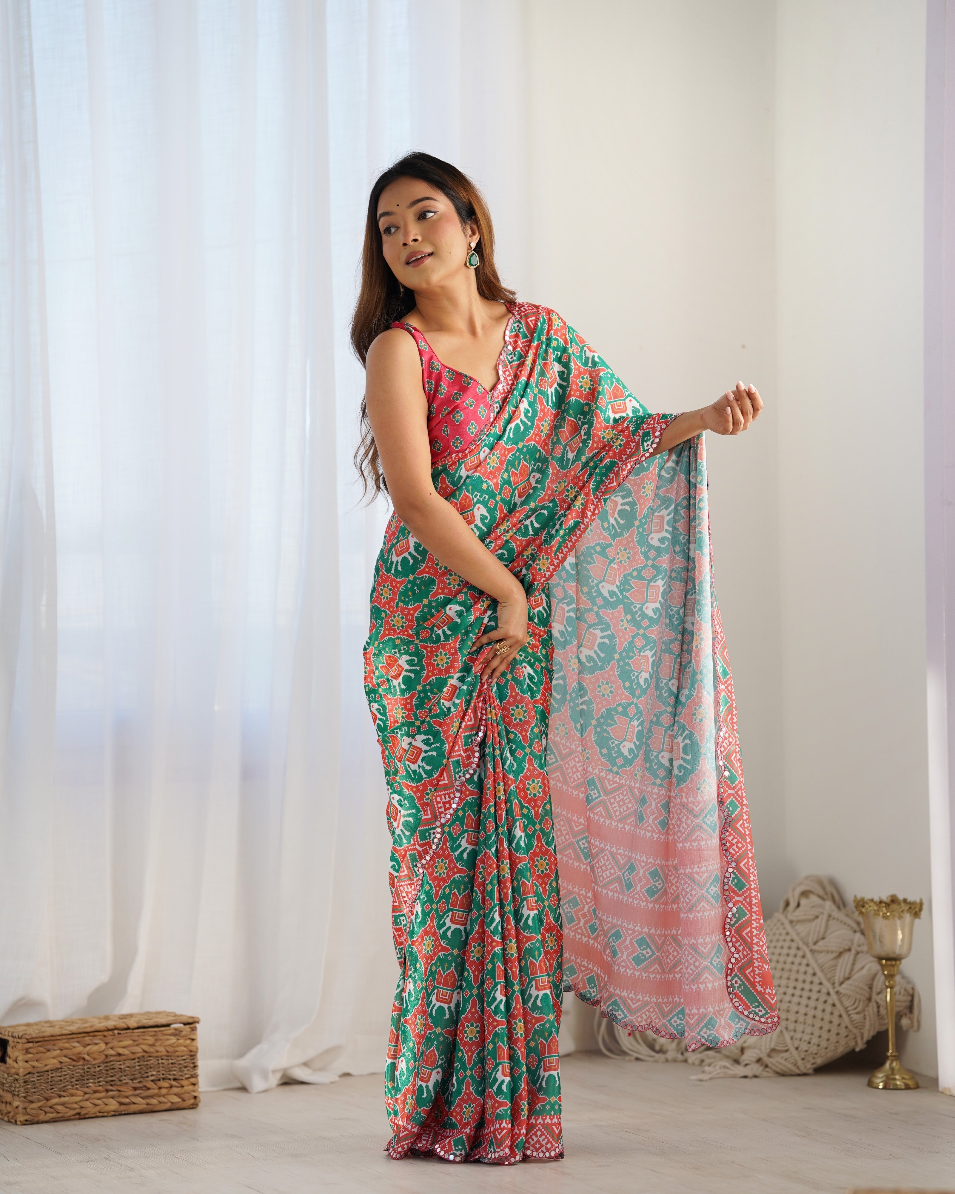 Woman wearing a floral saree in a bright room with white curtains.