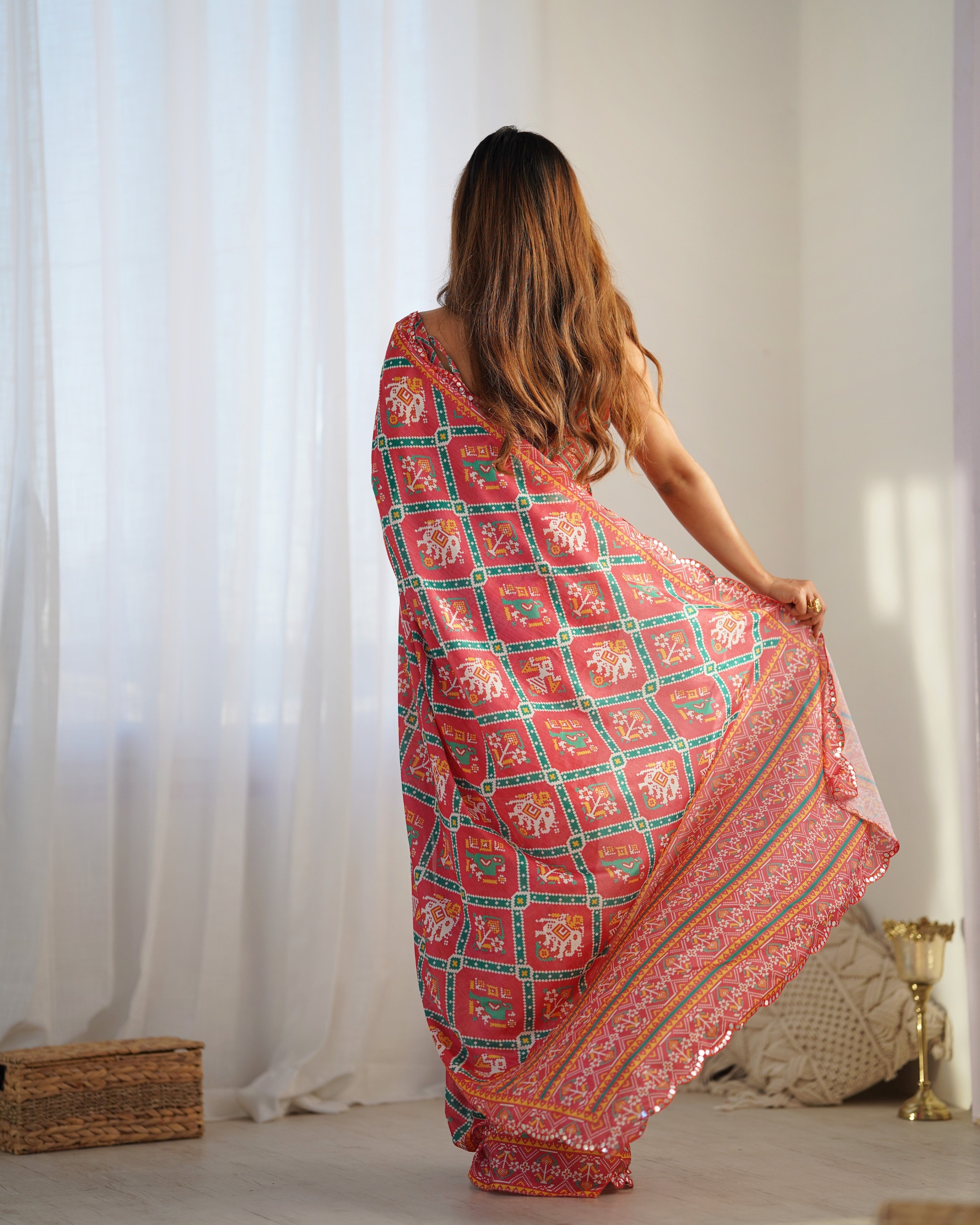 Woman wearing a pink and green patterned saree in a bright room.