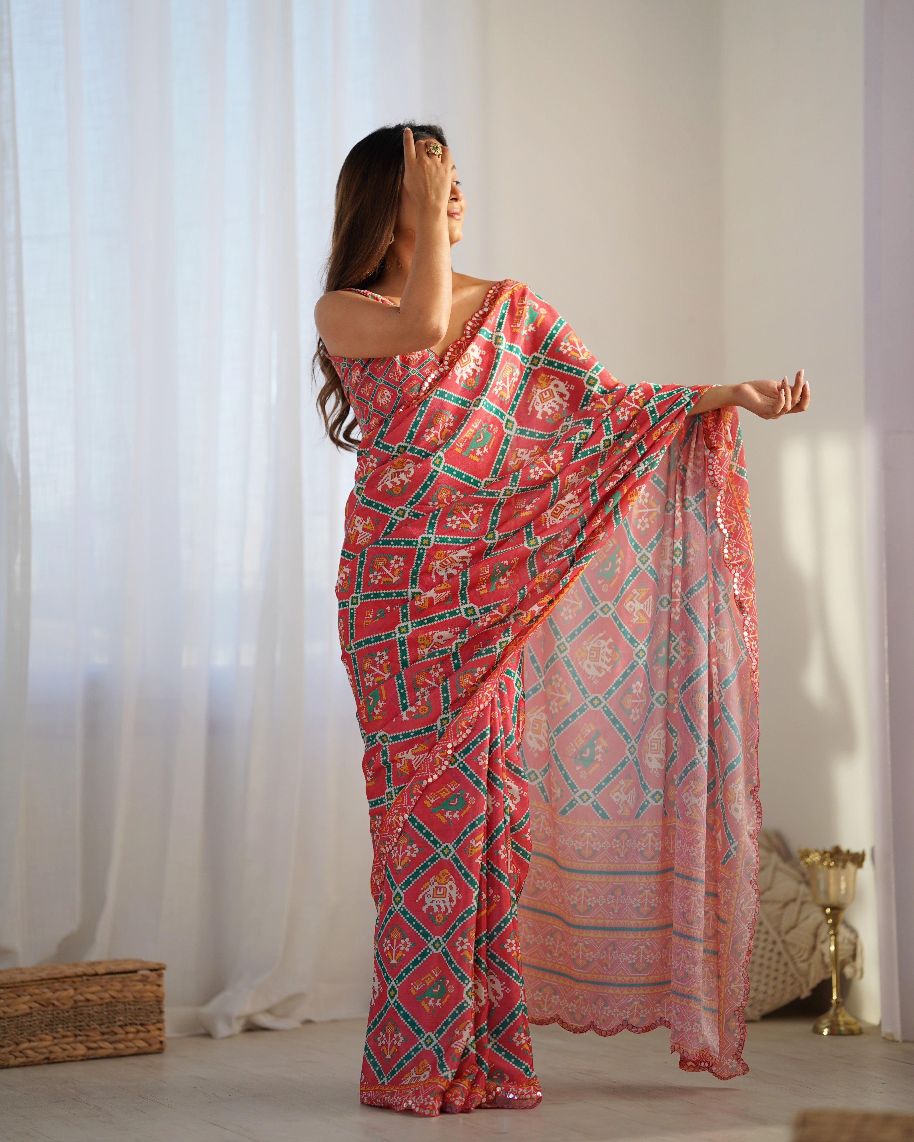 Woman wearing a pink and green patterned saree in a bright room.