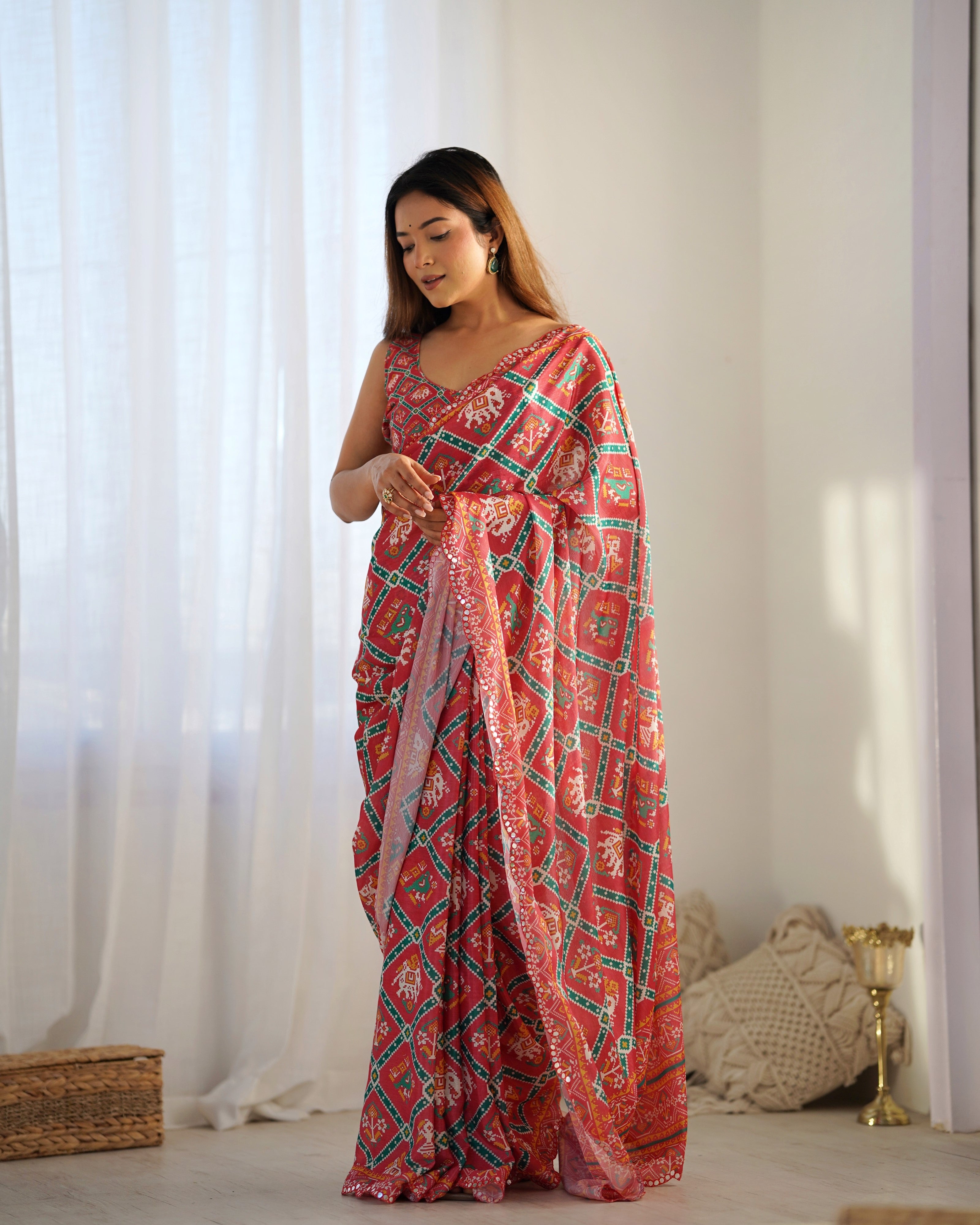 Woman wearing a pink and green patterned saree in a room with white curtains and a basket.