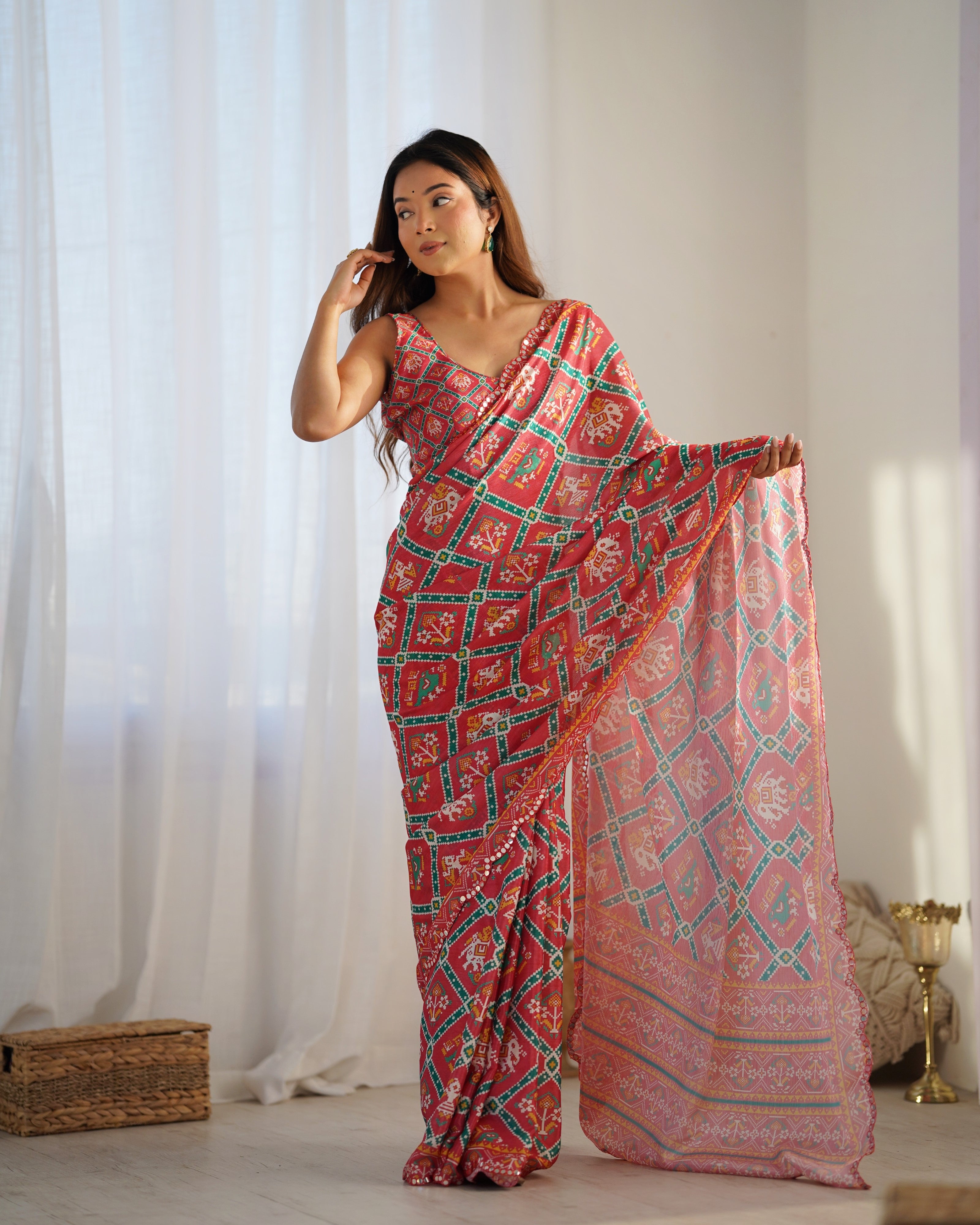 Woman wearing a pink and green patterned saree in a bright room.