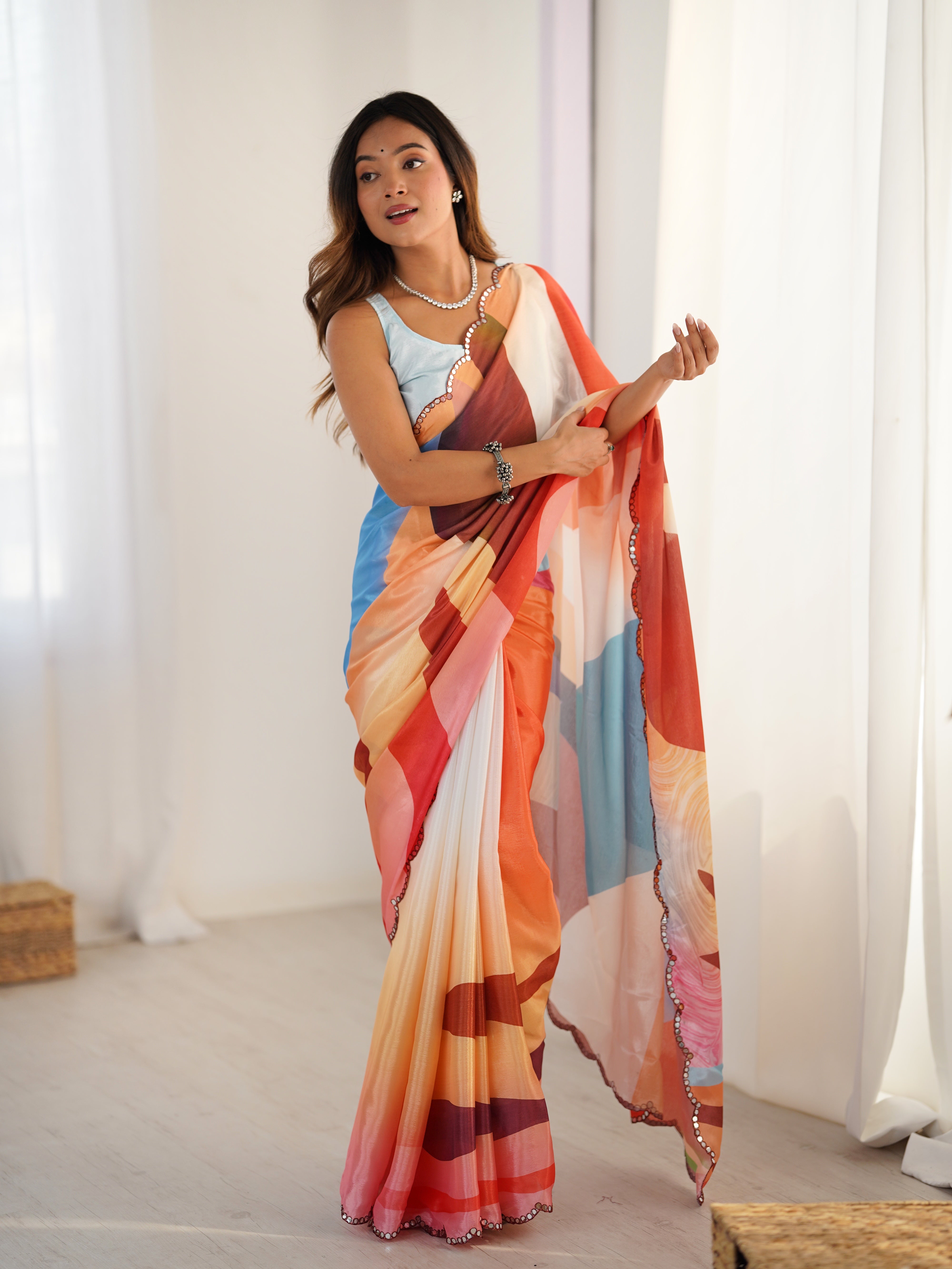Woman wearing a colorful saree with a pattern of vertical stripes in various colors against a white curtain background.