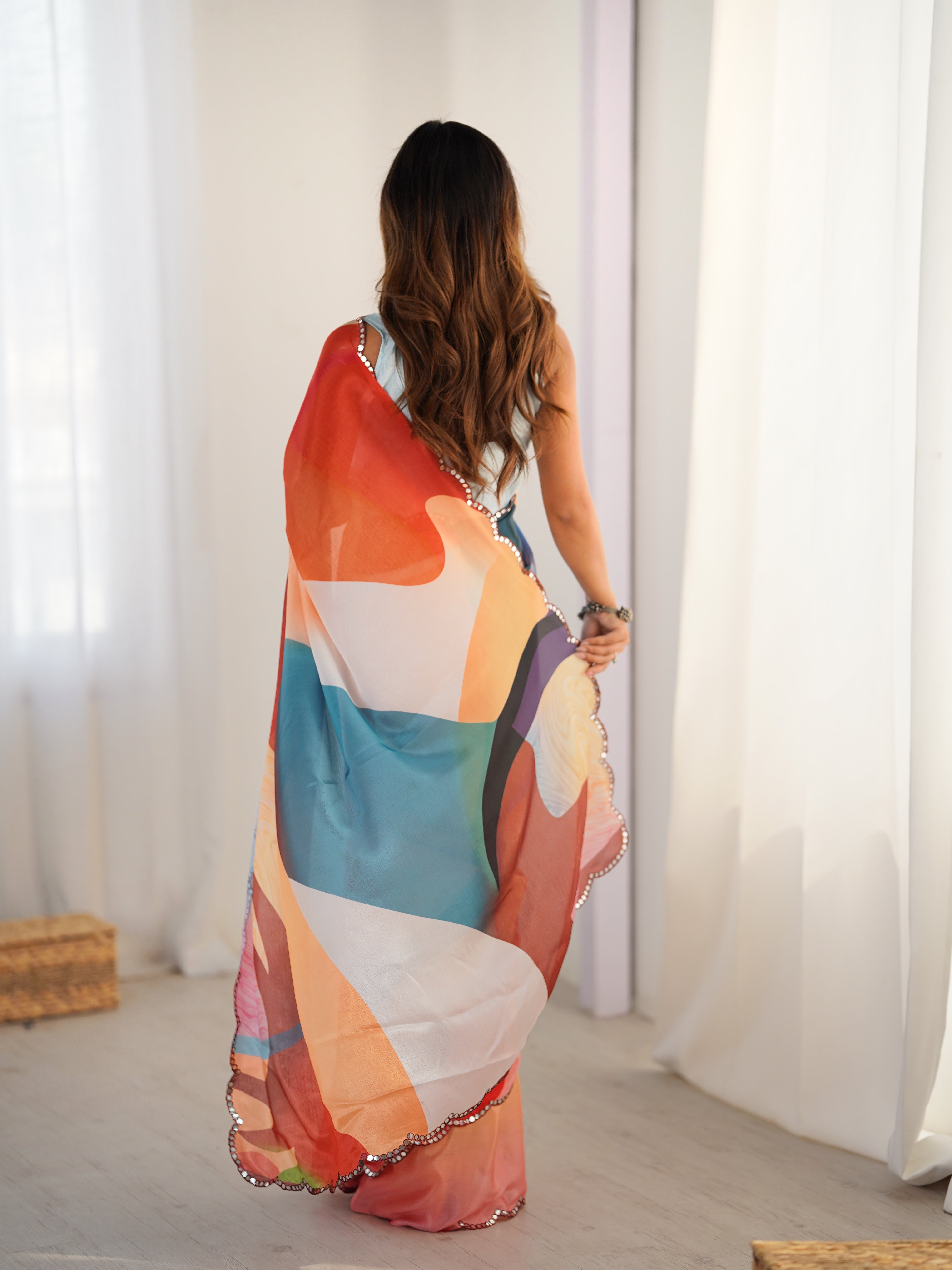 Woman wearing a colorful dress with abstract patterns in a room with white curtains.