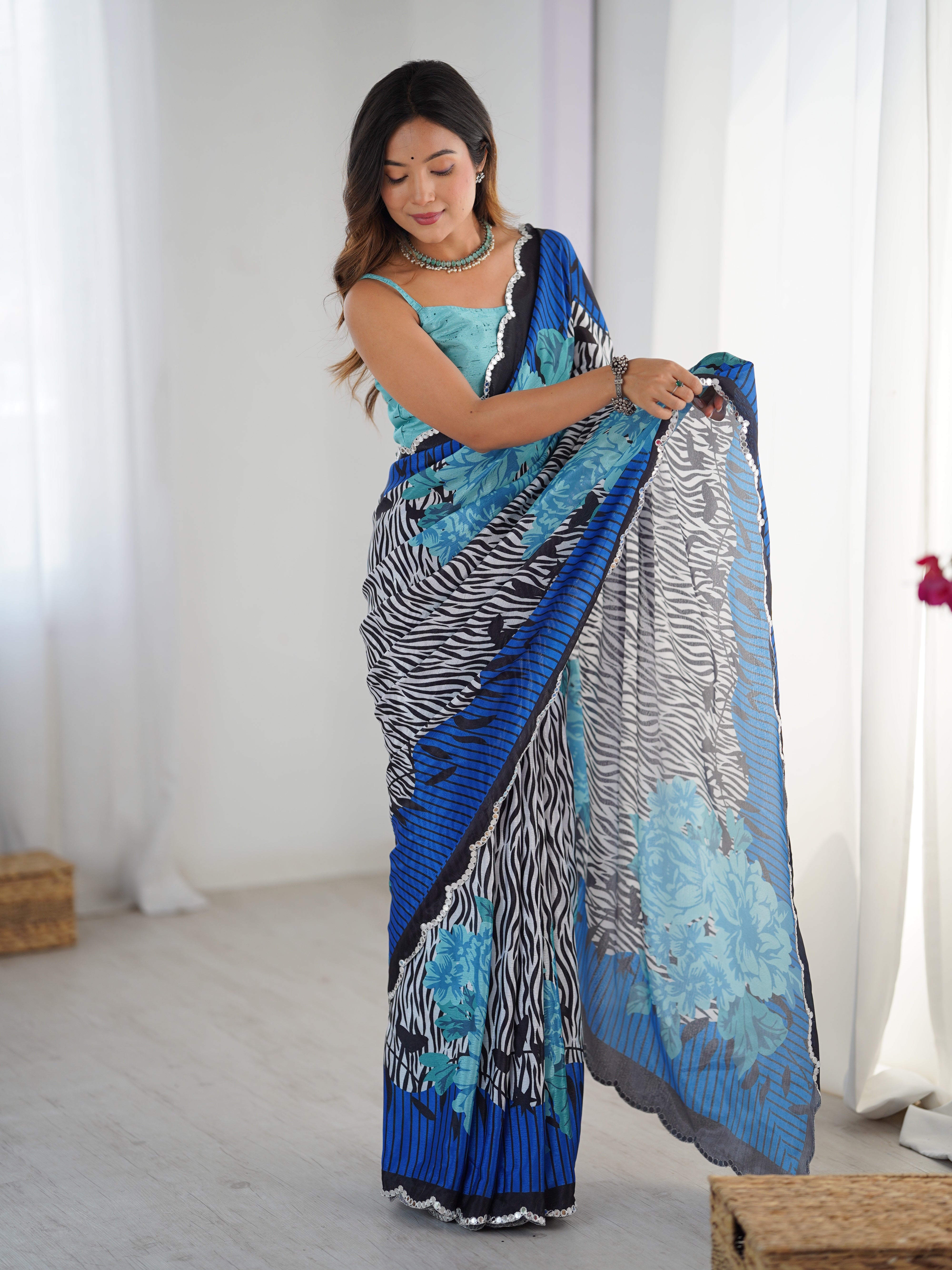 Woman wearing a blue and black patterned saree in a bright room.