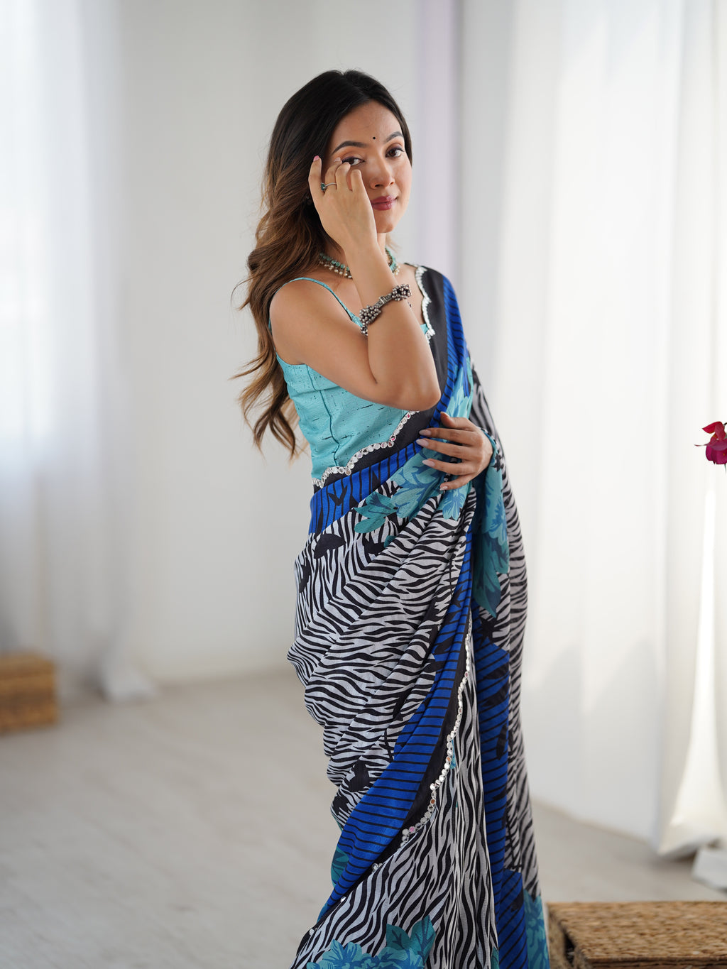 Woman wearing a blue and black patterned saree in a bright room.