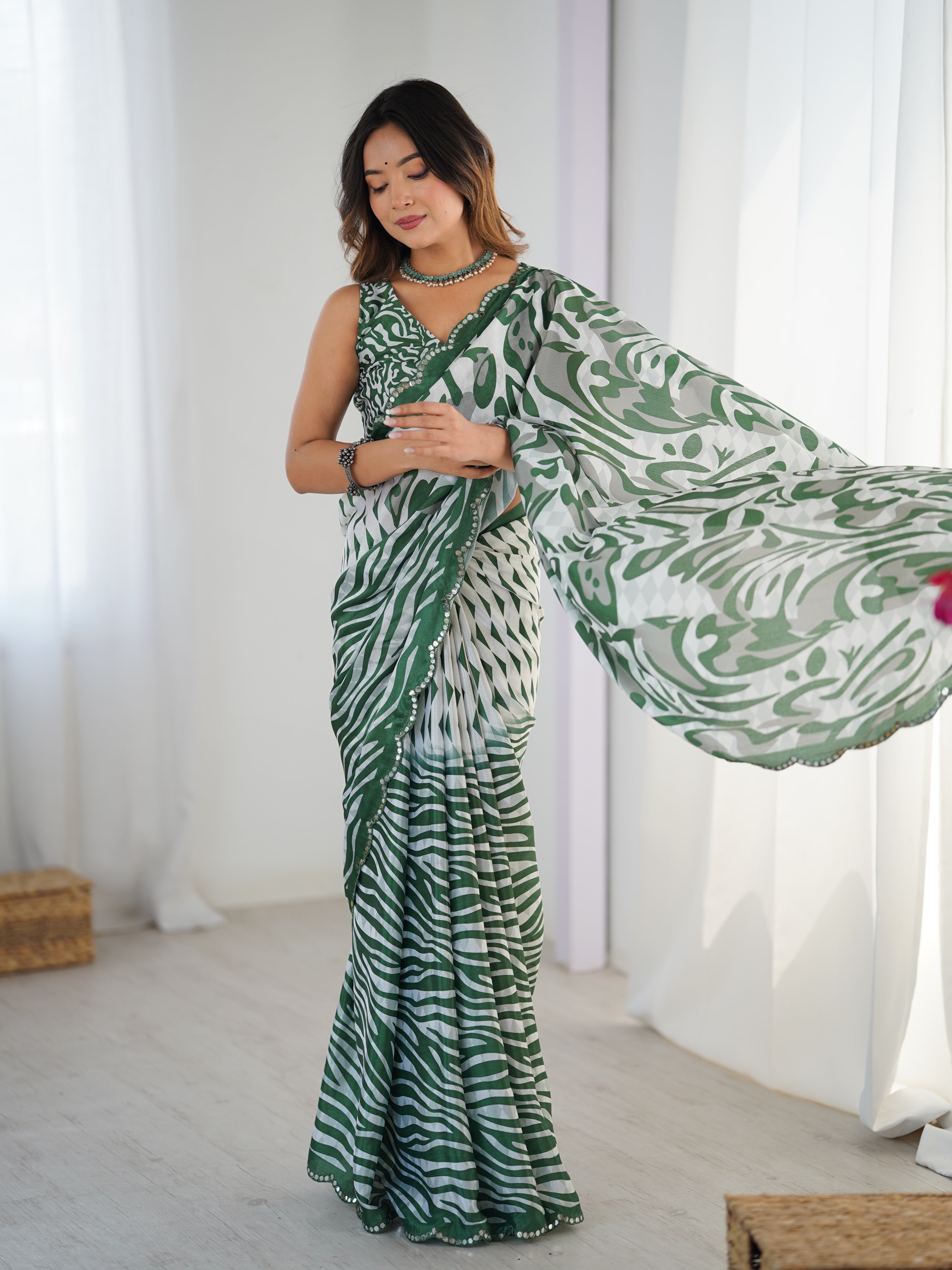 Woman wearing a green and white patterned saree in a bright room.