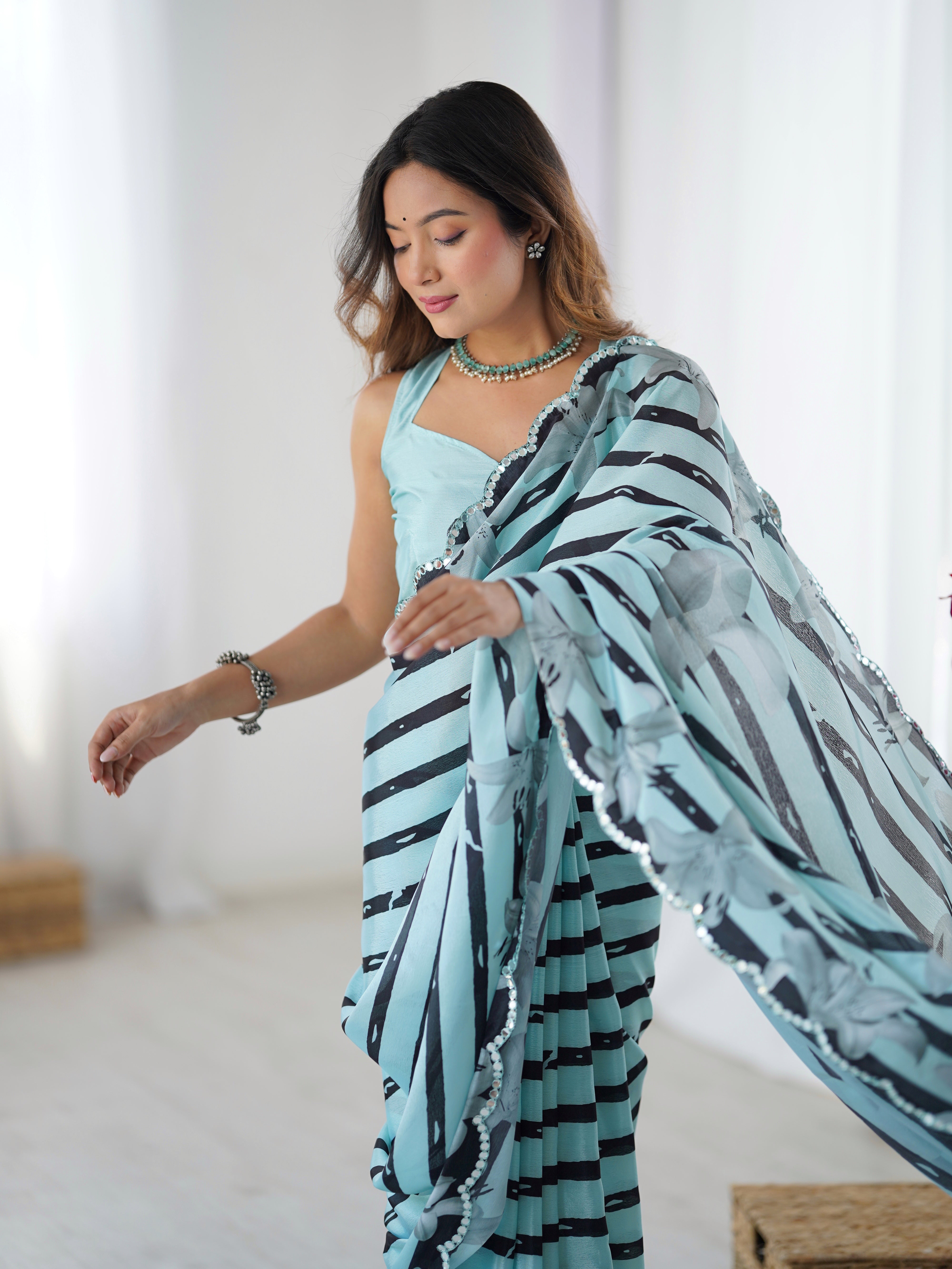 Woman wearing a light cyan saree with black patterns in a minimal indoor setting