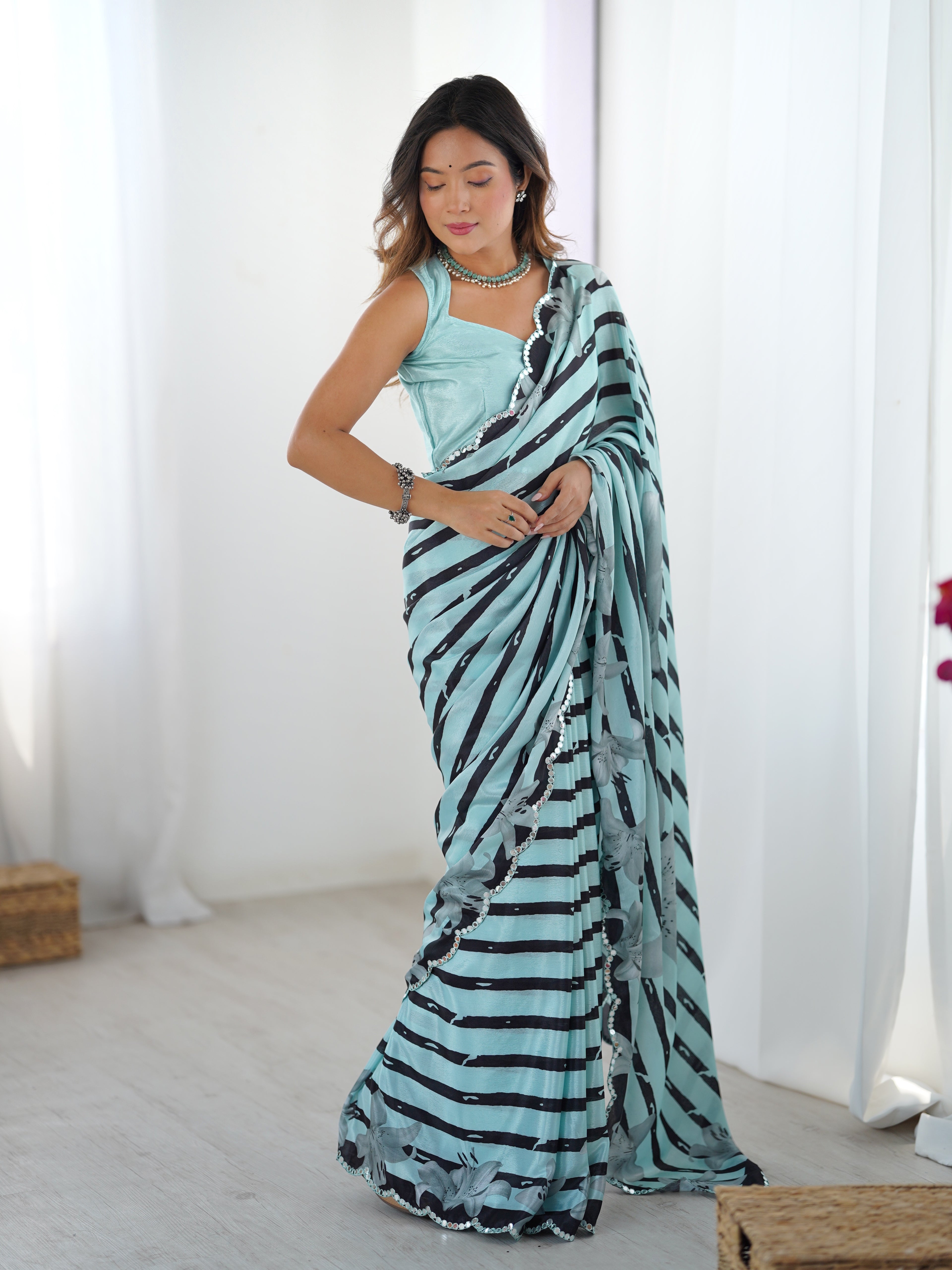 Woman wearing a light cyan saree with black patterns in a minimal indoor setting