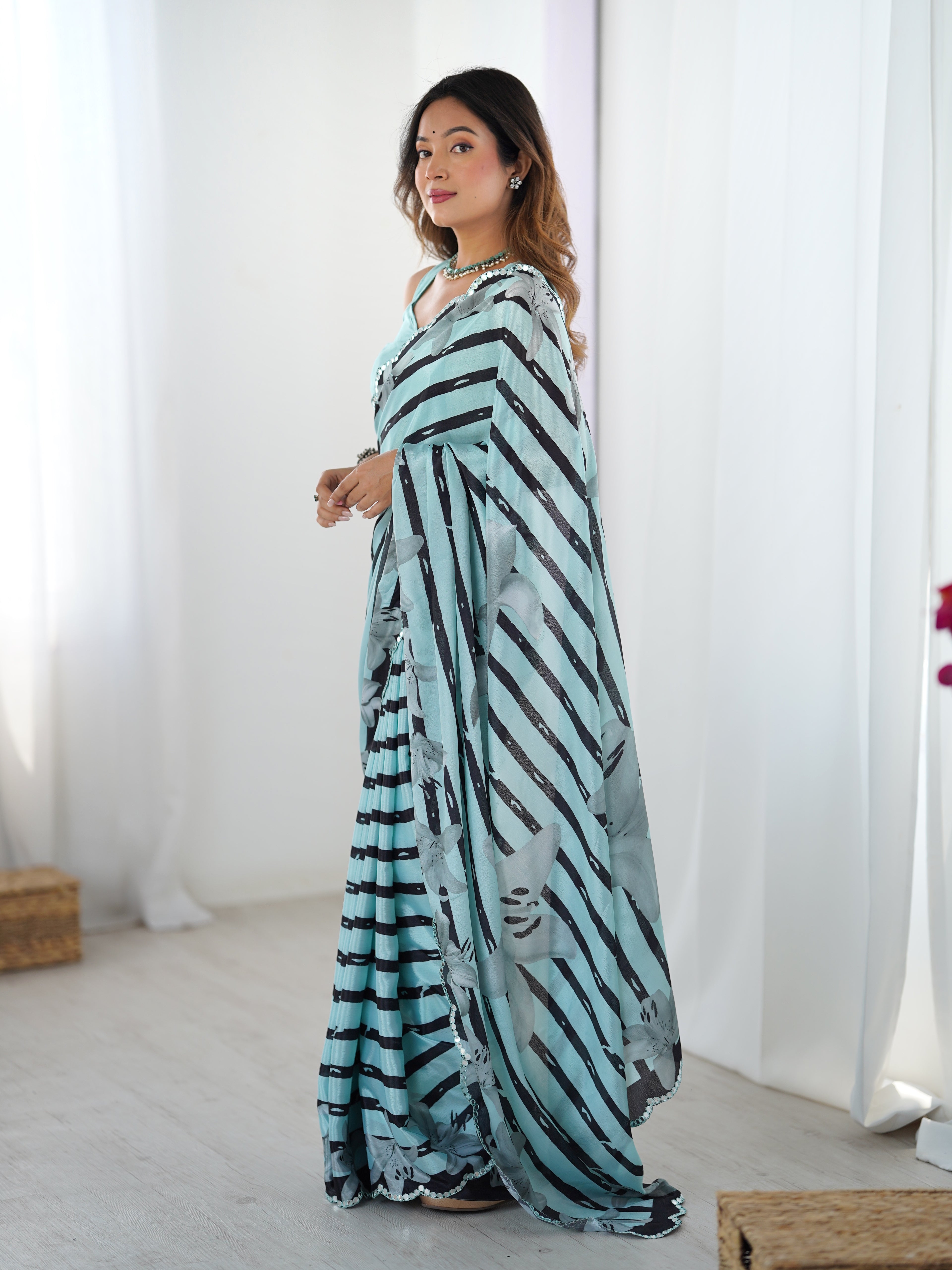 Woman wearing a light cyan saree with black patterns in a minimal indoor setting