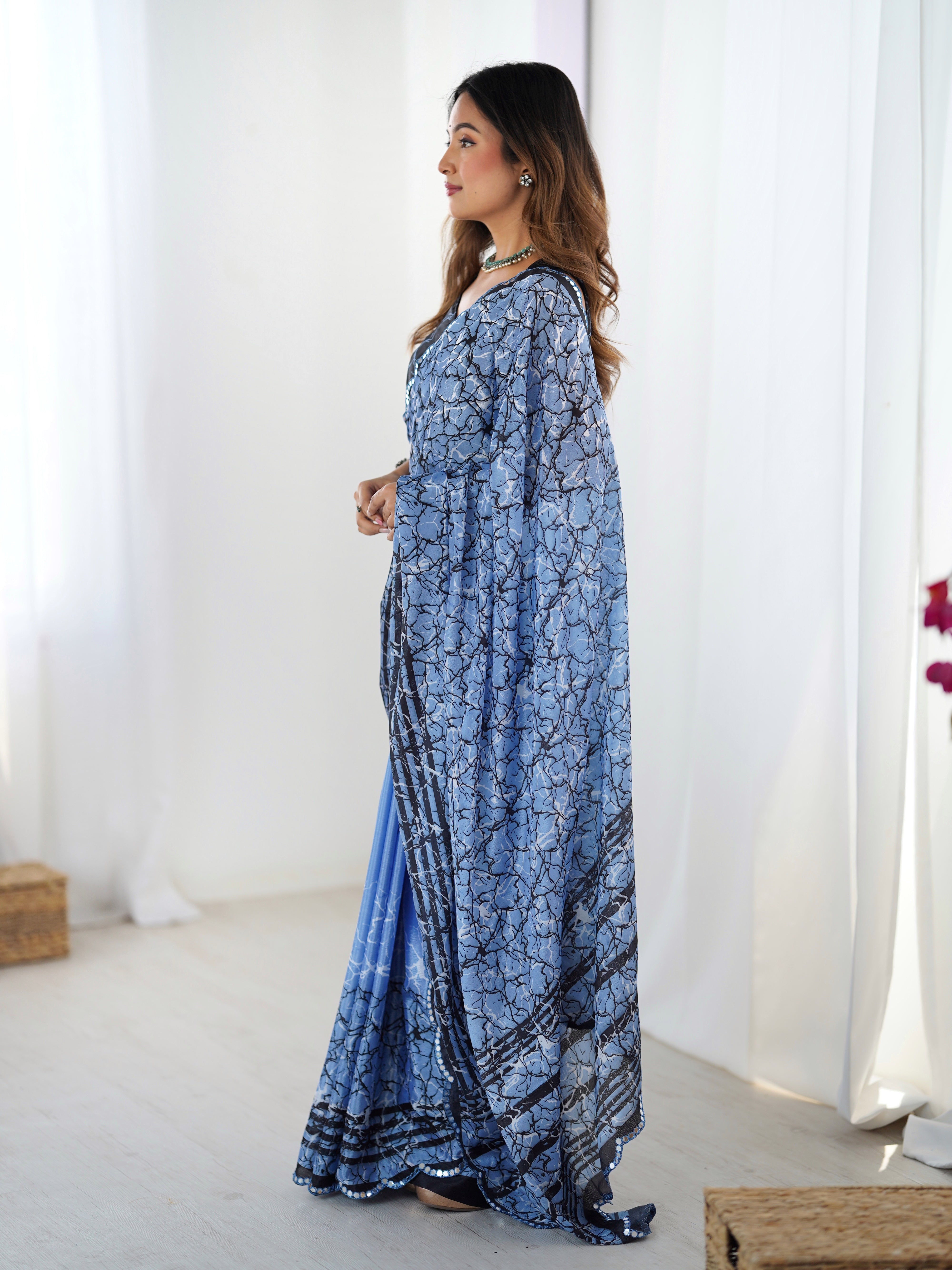 Woman wearing a sky blue patterned dress in a bright room with white curtains.