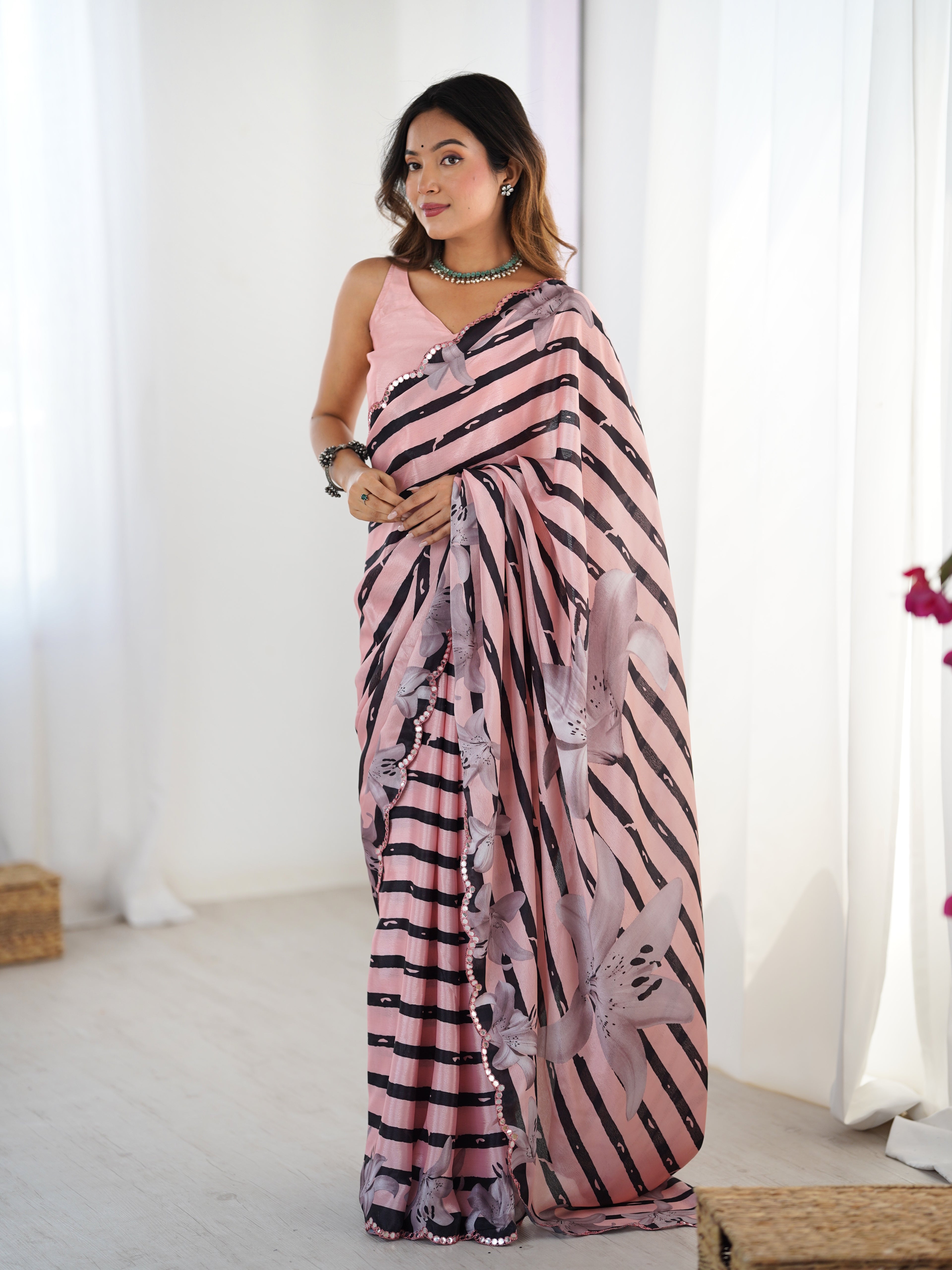 Woman wearing a pink and black patterned saree in a bright room.