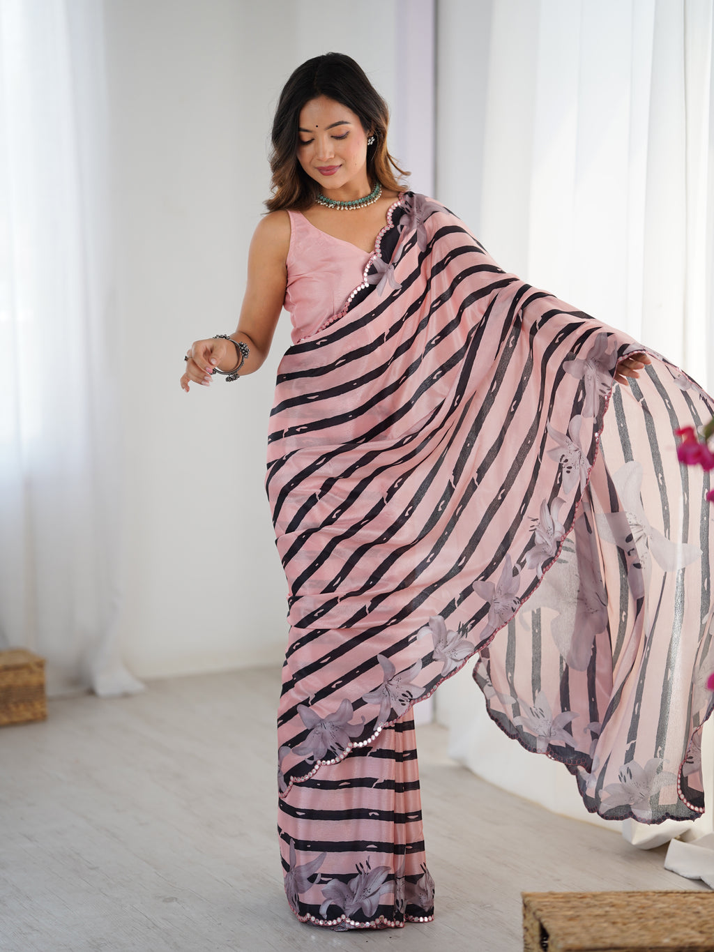 Woman wearing a pink and black patterned saree in a bright room.