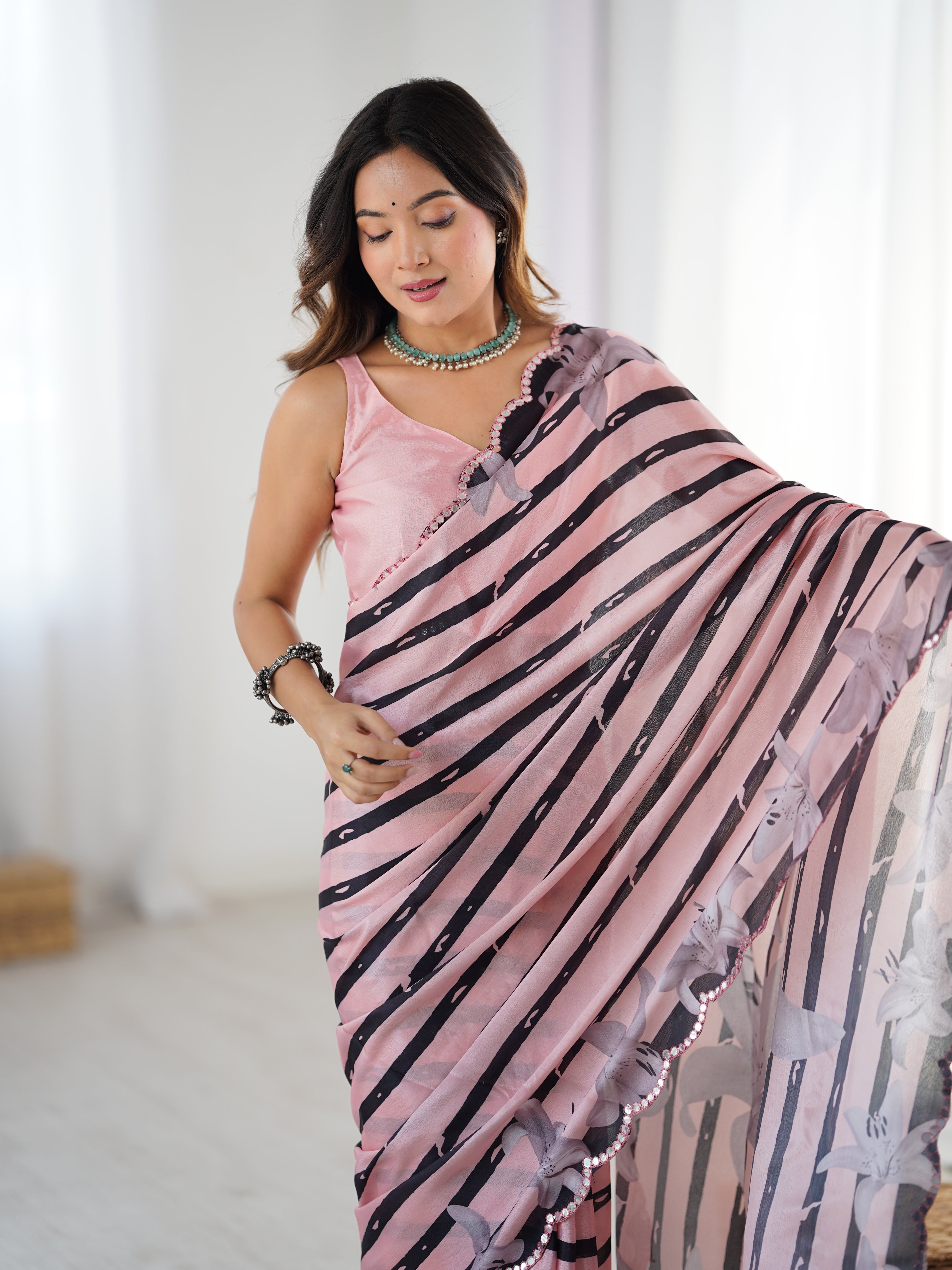 Woman wearing a pink and black patterned saree in a bright room.