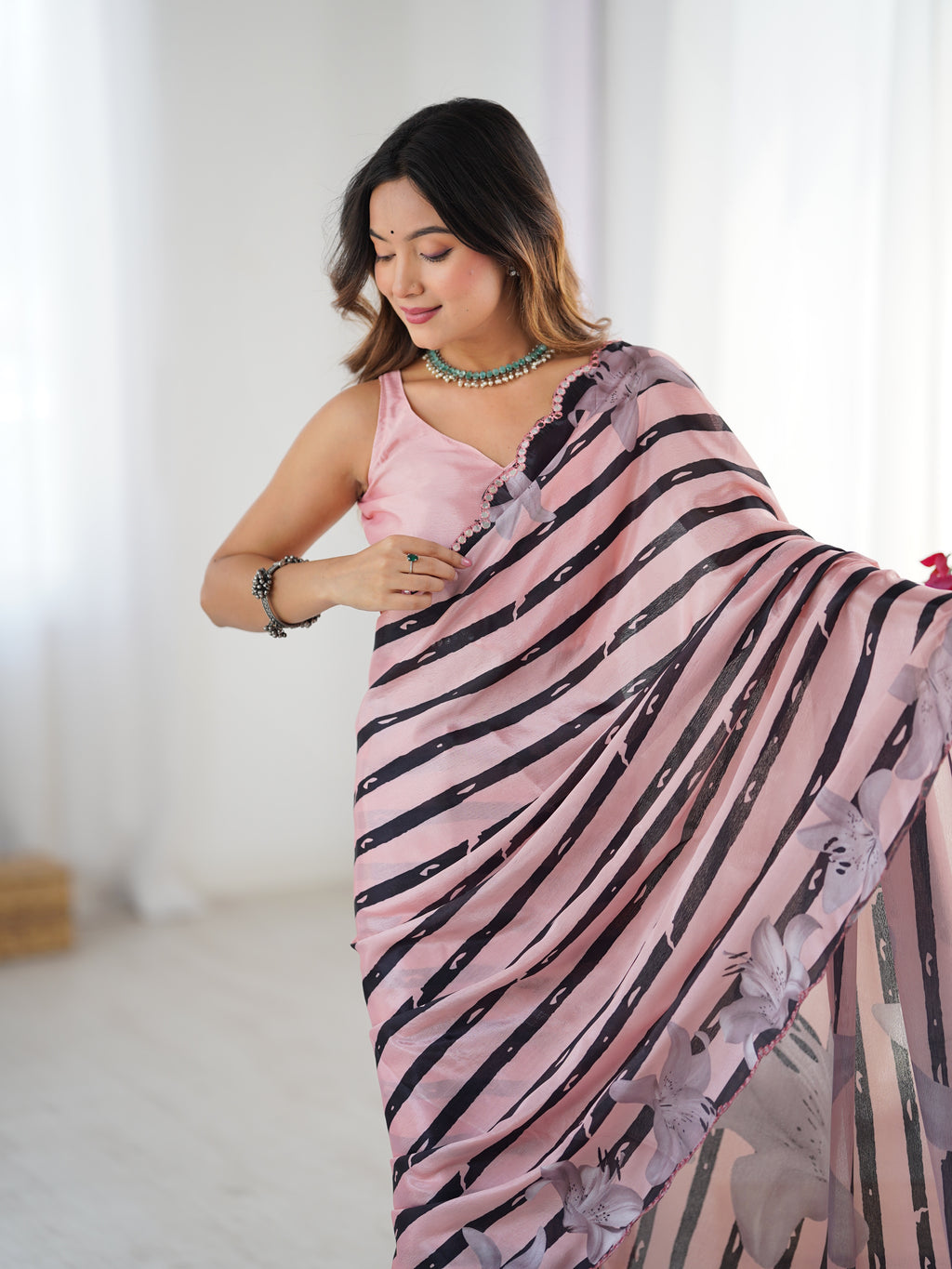 Woman wearing a pink saree with black floral patterns against a white background