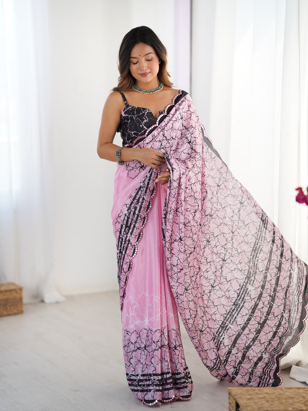 Woman wearing a pink and black patterned saree in a white room.