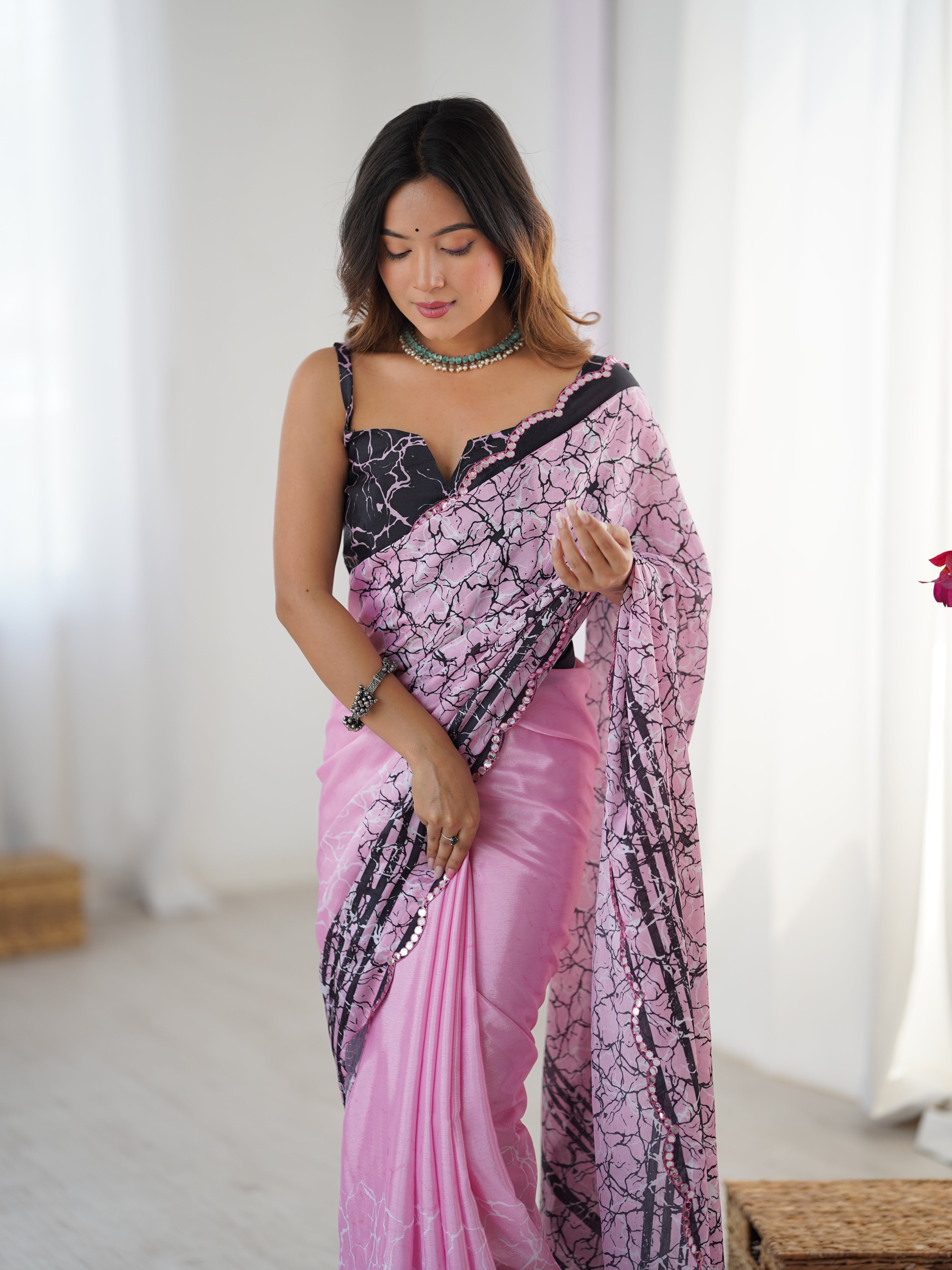 Woman wearing a pink and black patterned saree in a bright room.