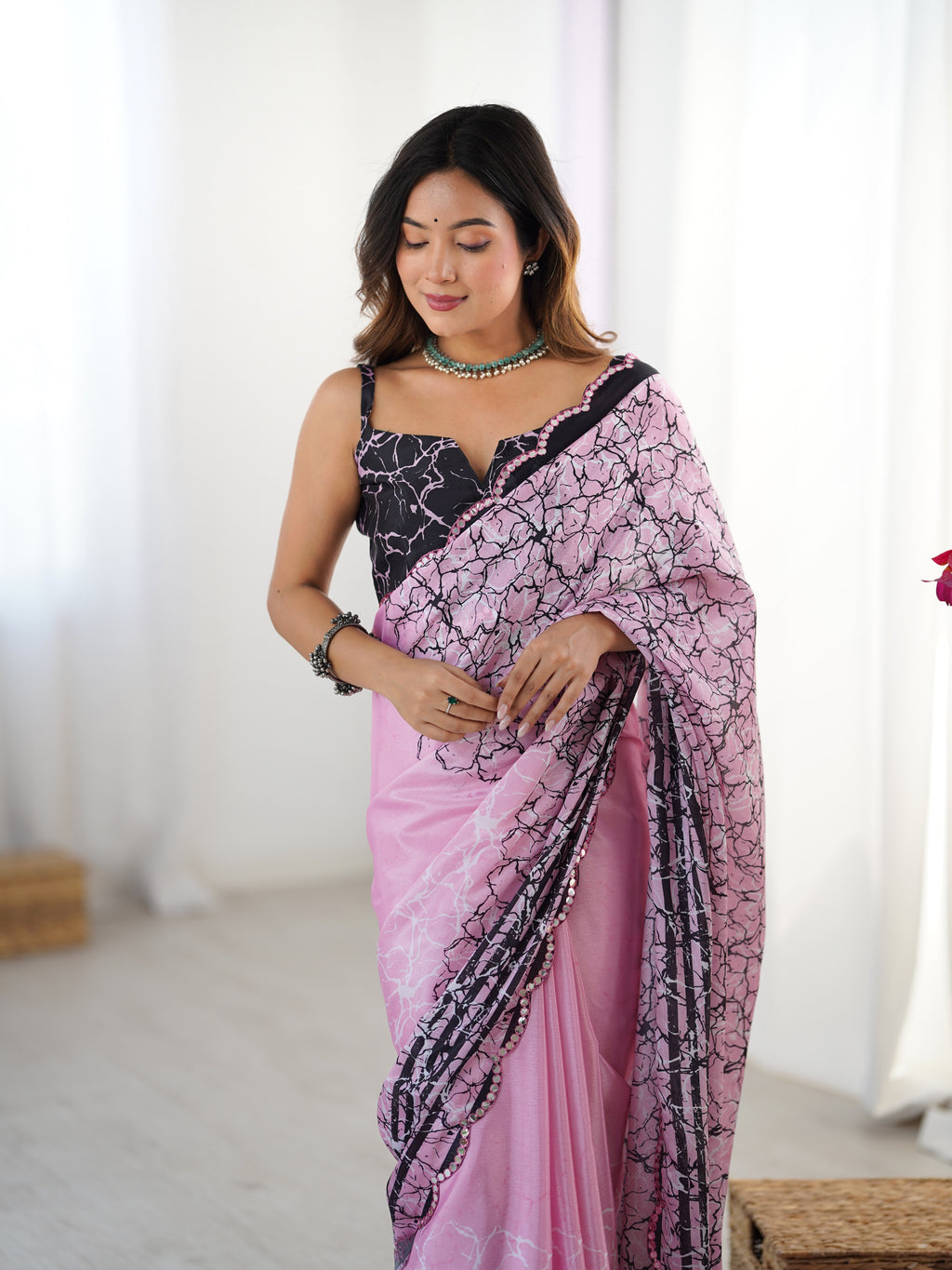 Woman wearing a pink saree with black patterns in a bright room.