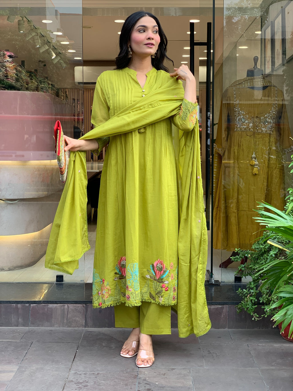 Woman in a green traditional kurta set outfit standing in front of a store window.