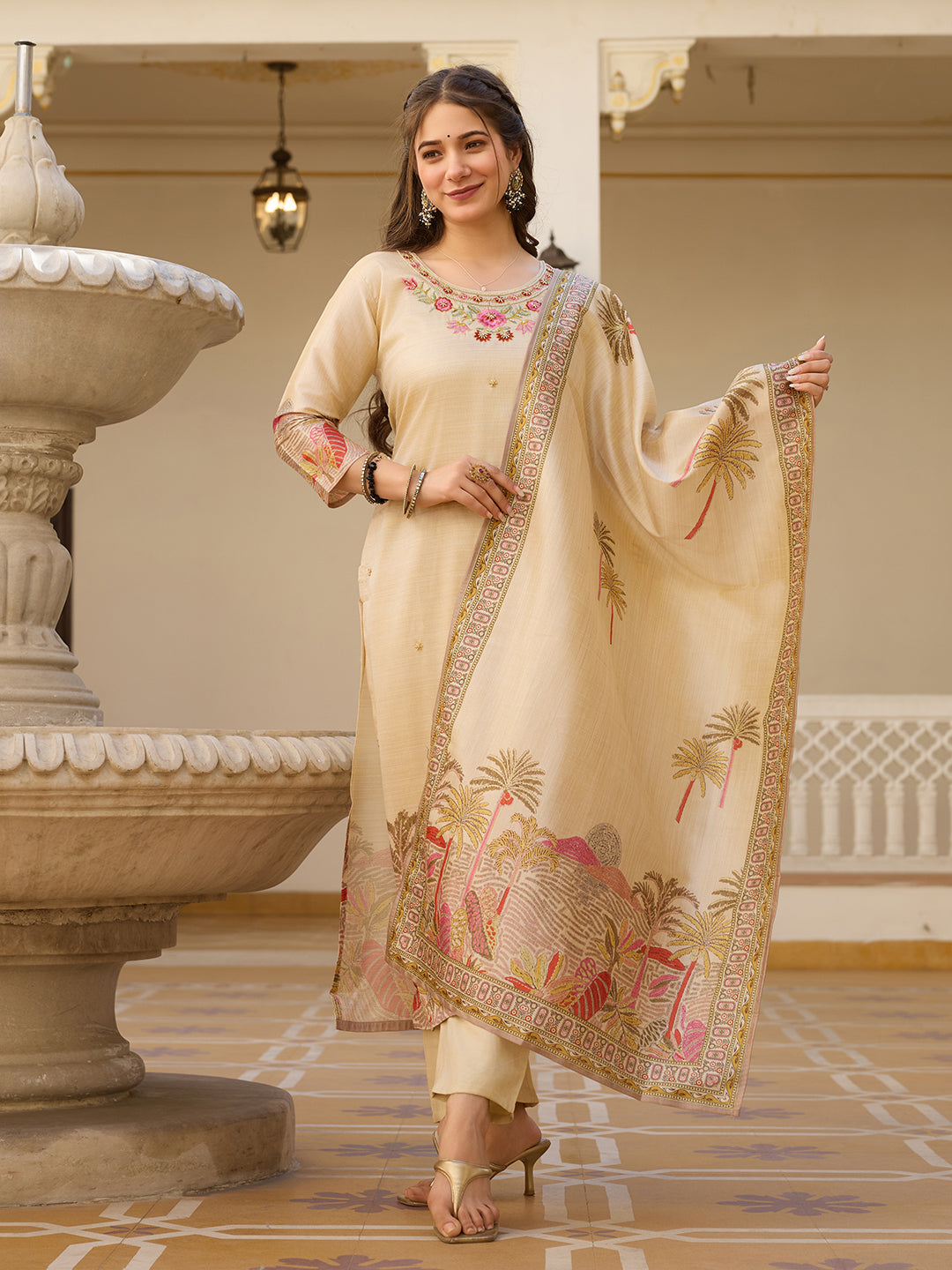 Woman in a cream-colored traditional outfit with floral patterns in an elegant indoor setting.