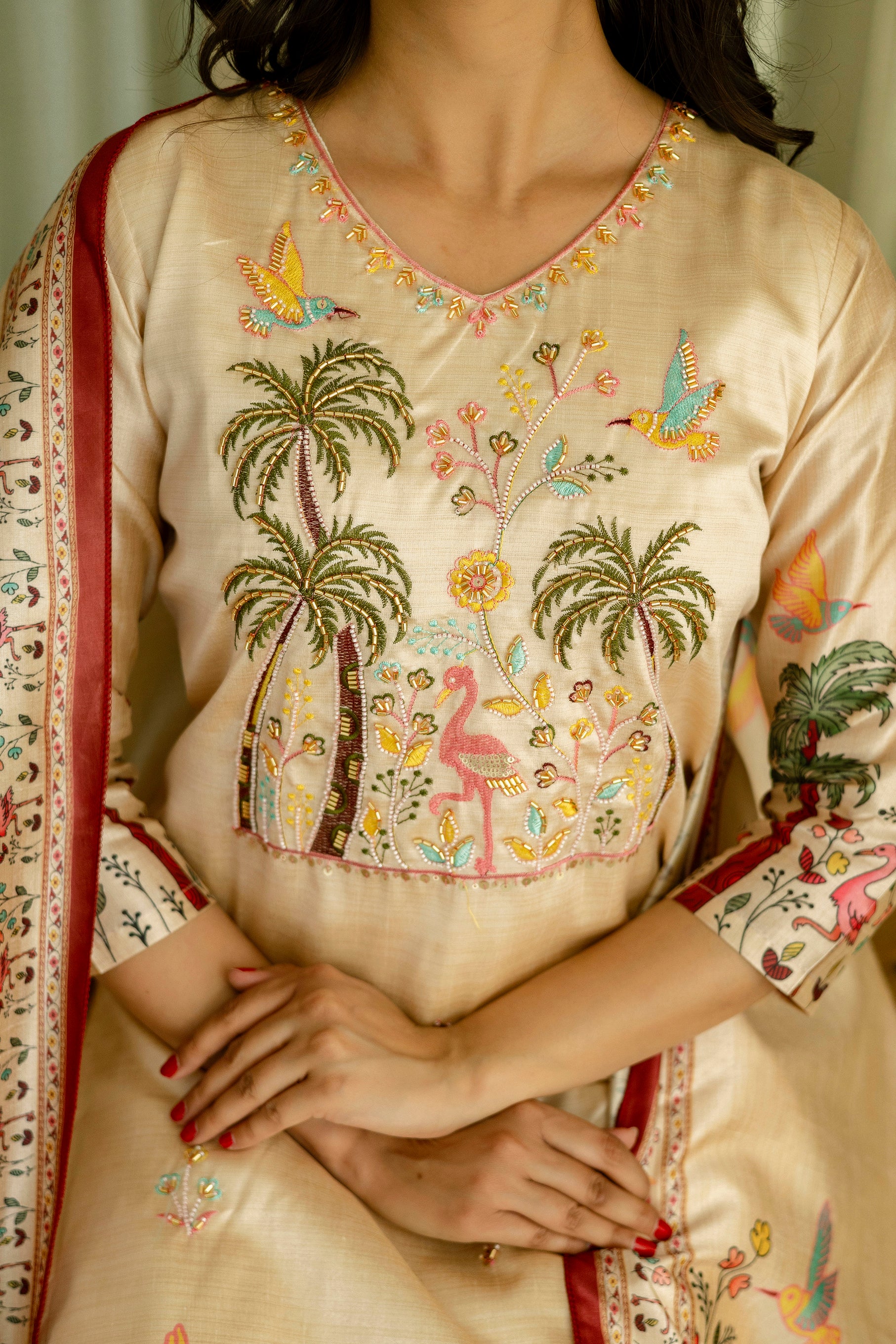 Beige embroidered kurta with floral and bird patterns, worn by a person.