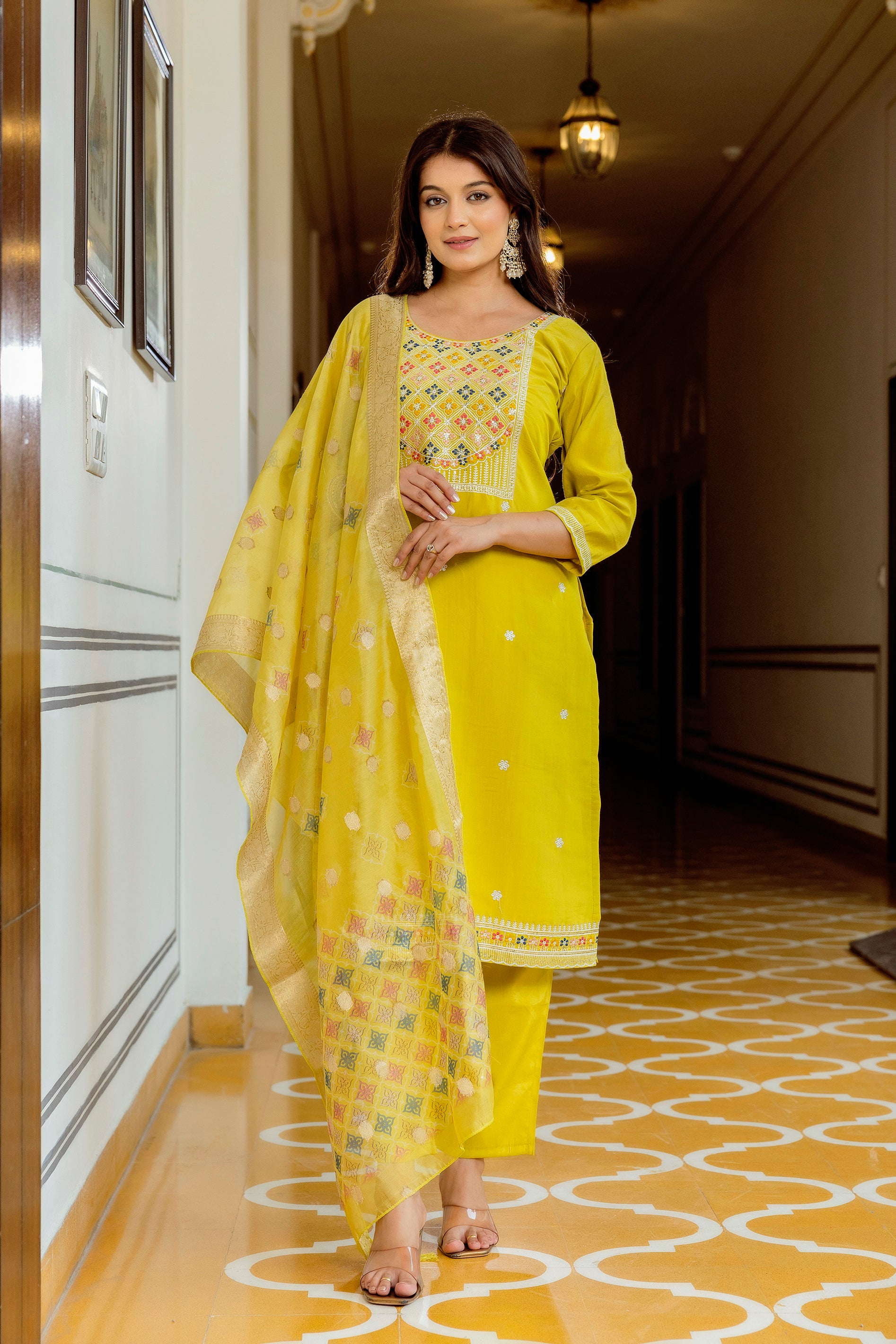 Woman in a yellow traditional outfit standing in a hallway with patterned floor.