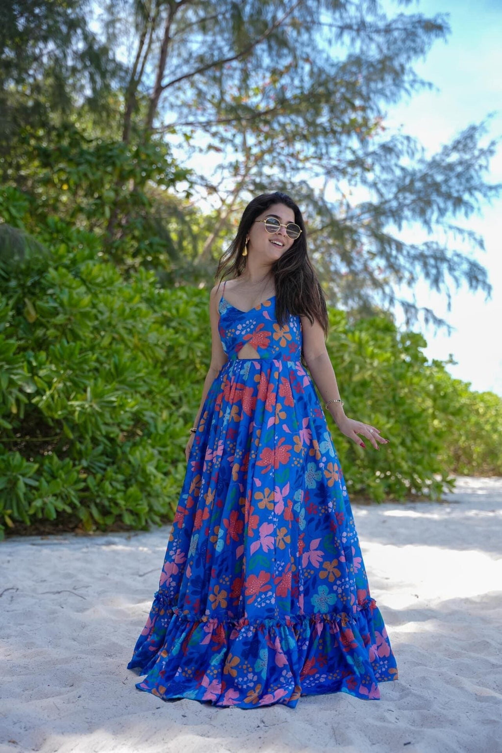 Woman in a blue poly rayon dress standing on a sandy path with greenery in the background