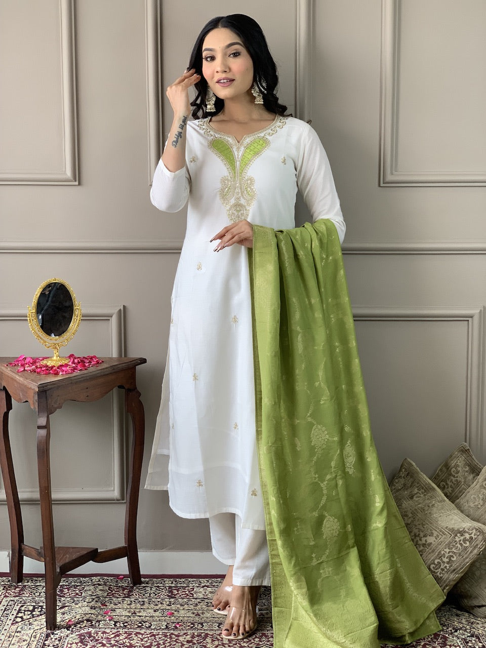 Woman in a white and green traditional outfit standing in a room with decorative elements.