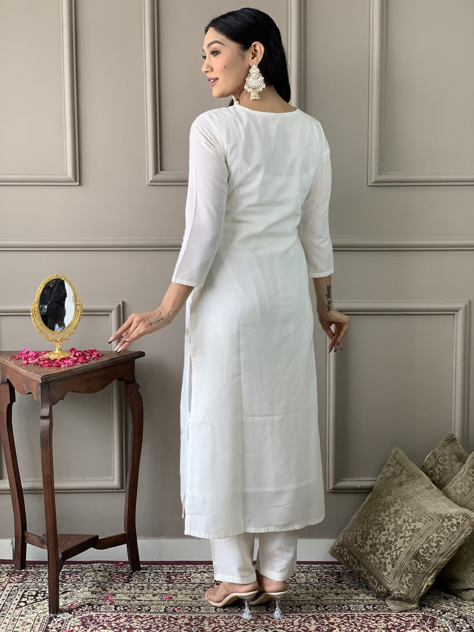Woman in a white kurta standing in a room with decorative elements.