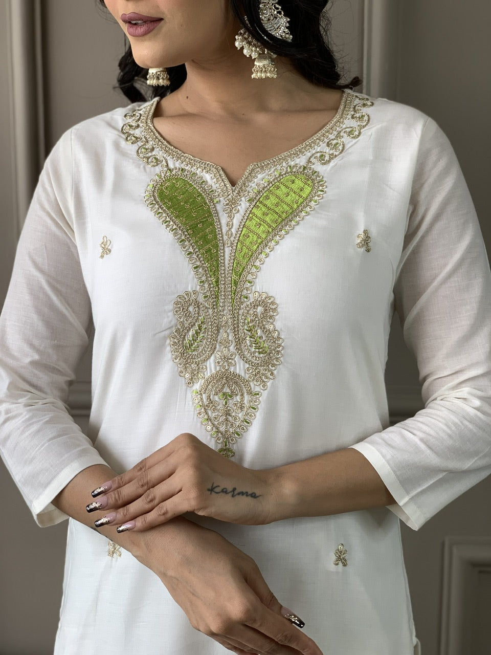 White kurta with green and gold embroidery on a plain background