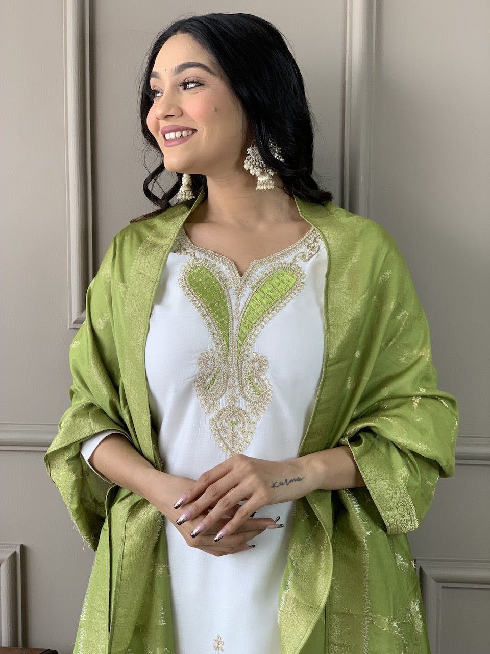 Woman wearing a white outfit with green shawl against a neutral background