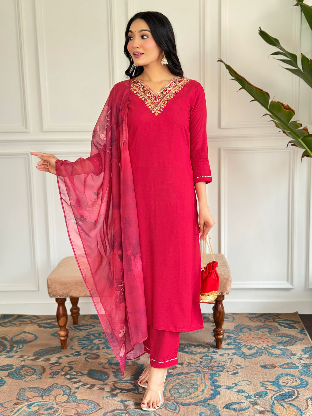 Woman in a red traditional outfit with a matching dupatta standing in a decorated room.